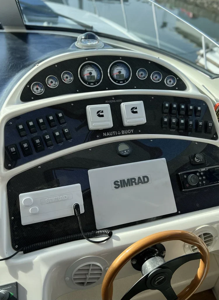 Boat dashboard with gauges, switches, and electronic equipment, including a SIMRAD display and control panel.