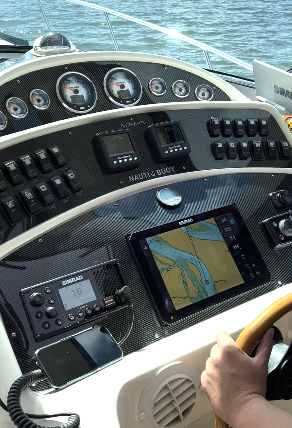 The interior of a boat's control panel showing navigation equipment, gauges, switches, and a person steering.