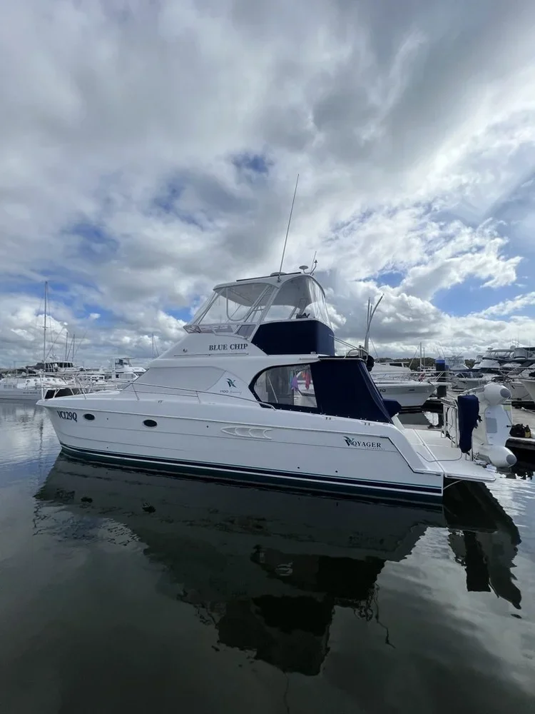 A white motor yacht named BLU CHIP docked at a marina with other boats, under a partly cloudy sky.