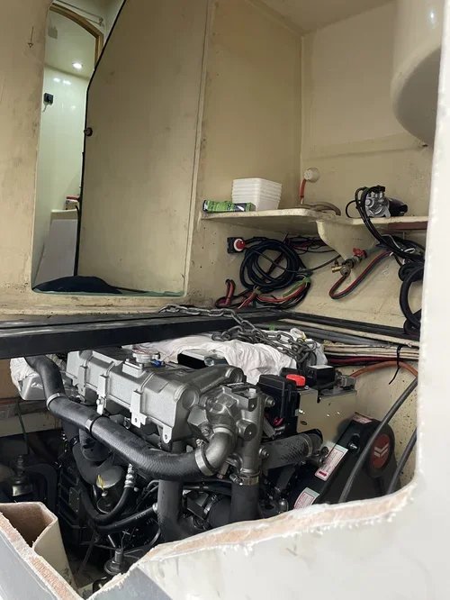 View of an engine installed inside a small, confined space in a boat or RV, with wiring and a mirror reflecting a bathroom or shower area.