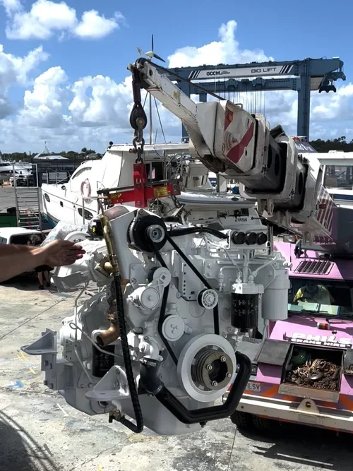 A large industrial engine being lowered with a crane at a marina. The crane is labeled "GCCM" and "BIG LIFT," and part of a boat is visible in the background.