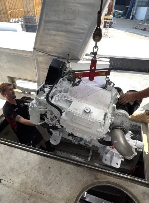 Two workers installing a large industrial engine in a construction site with a concrete floor and structure.