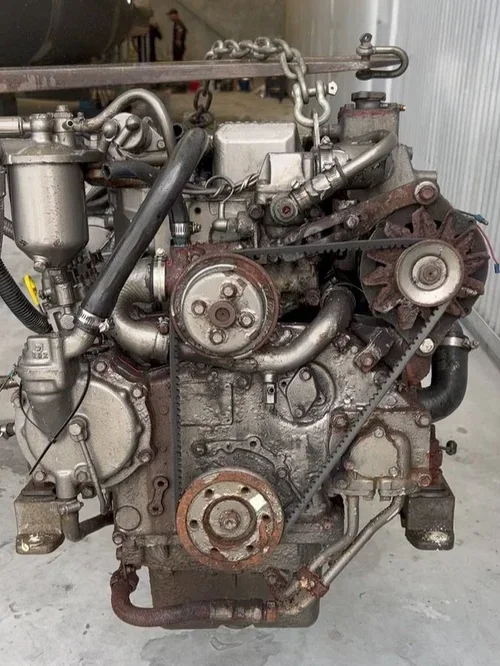 A used car engine with visible belts, pulleys, hoses, and metal components, placed inside a garage or workshop.