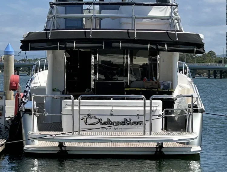 Rear view of a white yacht docked at a marina, with a black canopy and railing, and the name 'Destraction' written on the stern, near Sydney.