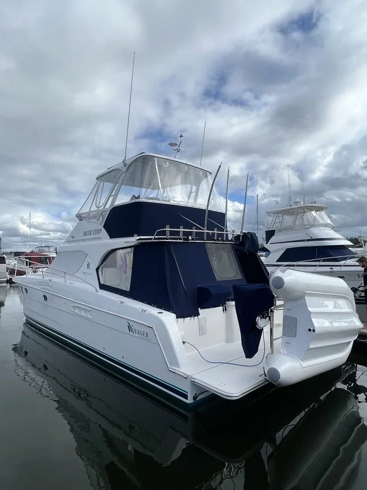 A white yacht named 'Blue Chip' docked at a marina, with other boats and a cloudy sky in the background.