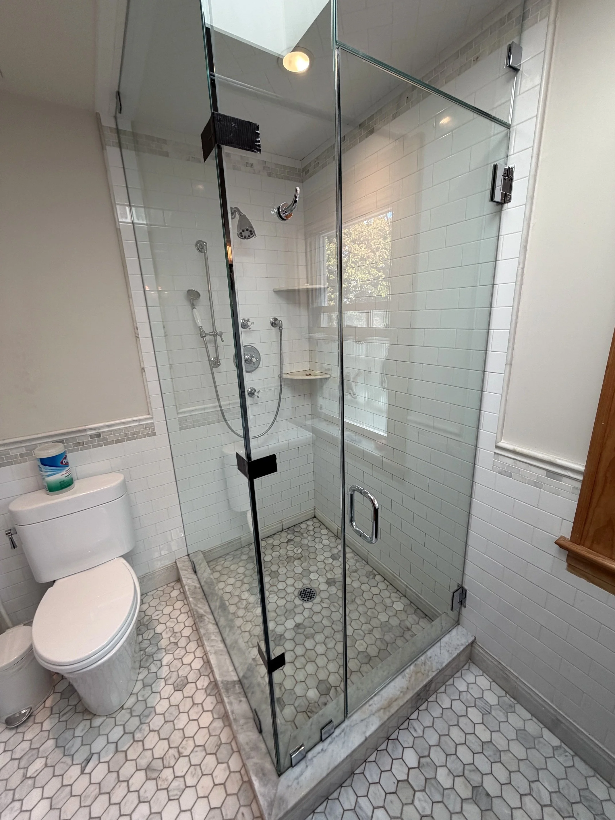 Modern bathroom with glass-enclosed walk-in shower, white subway tile walls, hexagon floor tiles, and toilet