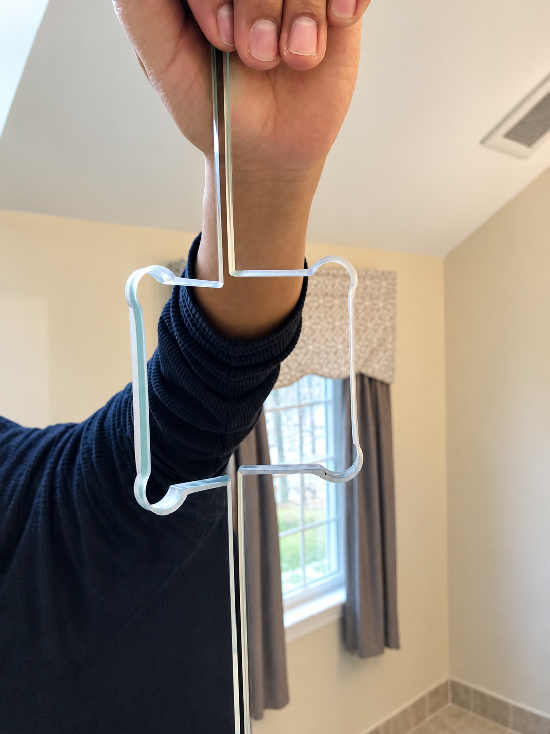 Hand holding a clear acrylic shower door sweep seal with hooked edges