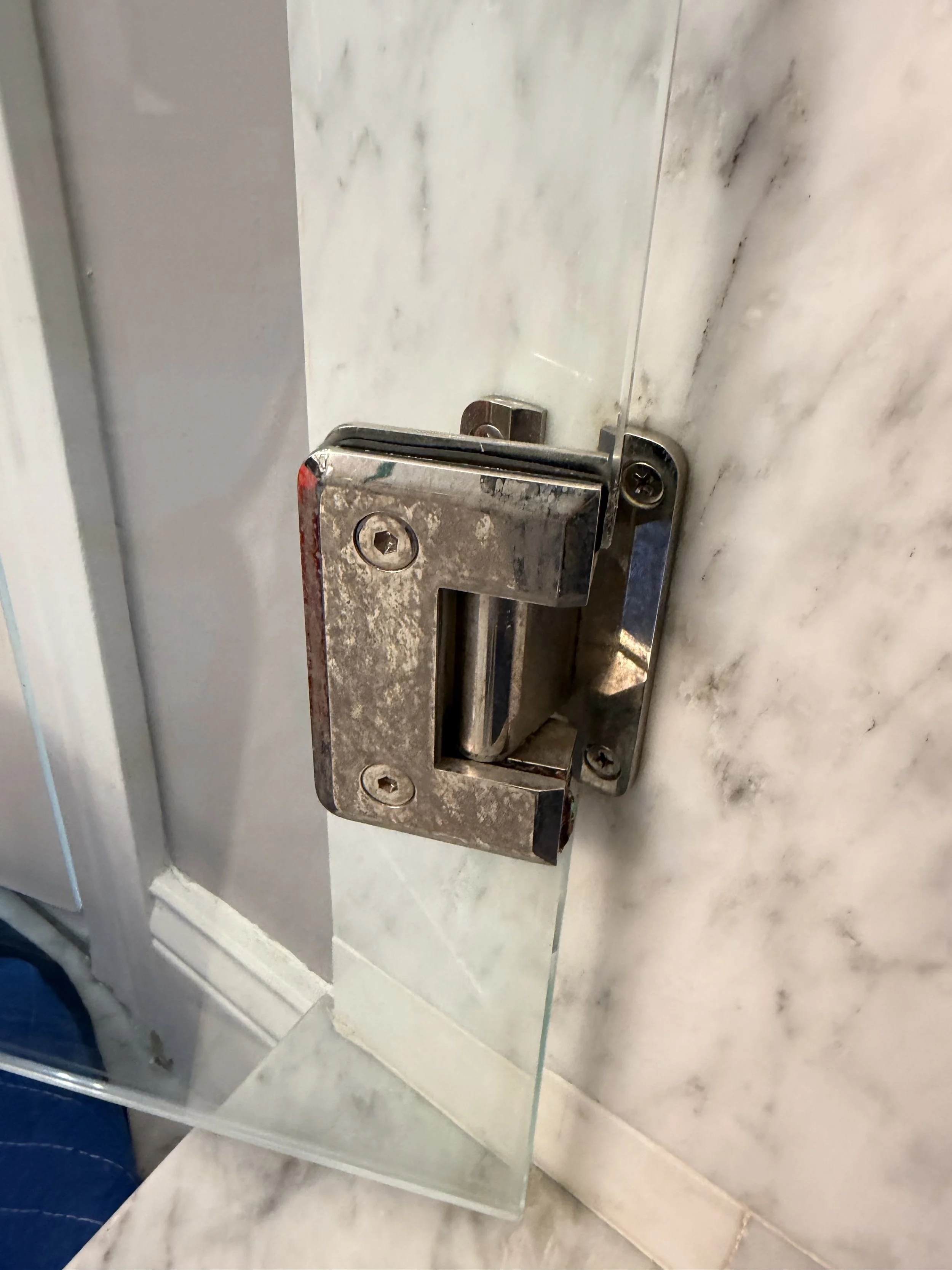Close-up of a tarnished metal door latch and lock mounted on a marble wall.