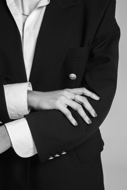 Close-up of a marketing person in a black suit with a white shirt, crossing their arms. The person is wearing a ring and the background is plain.