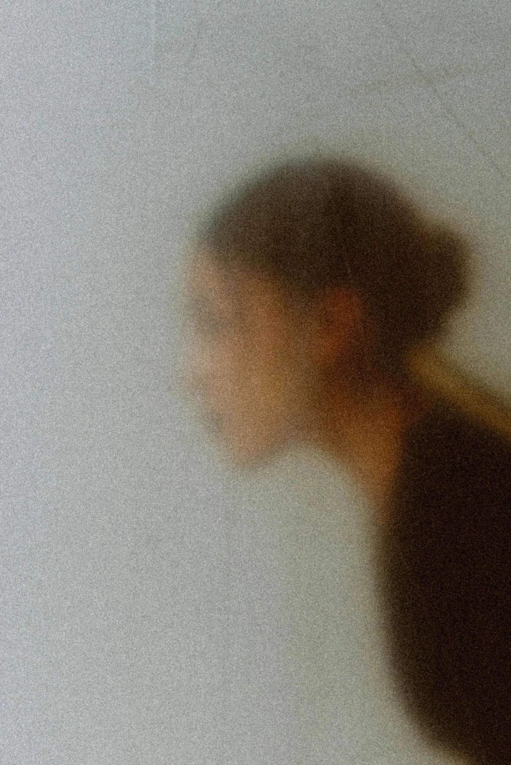A blurred, close-up shot of a person's face with a background that appears to be a plain white or light-colored surface.