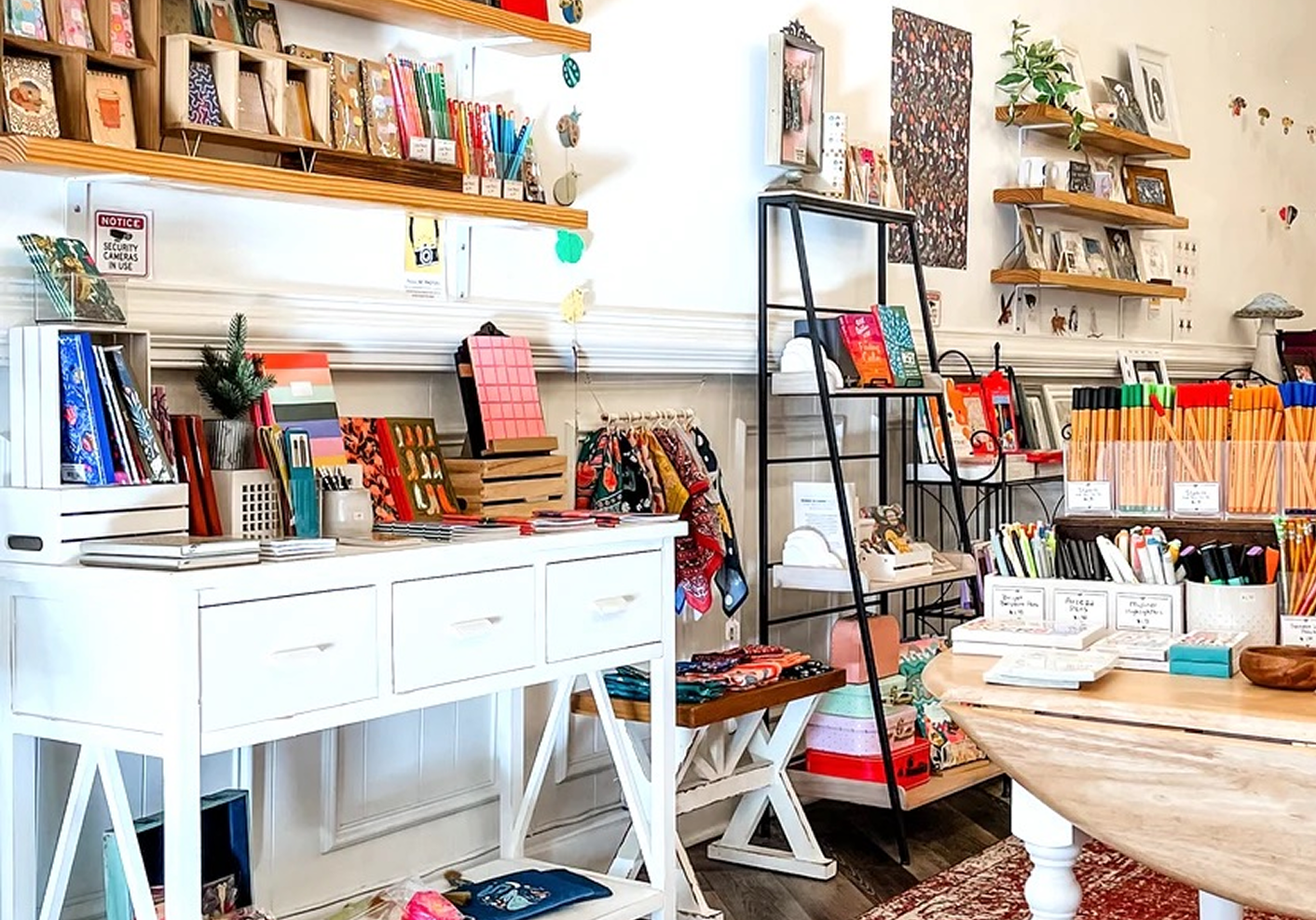 Decorative store display with notebooks, pens, and stationery items on shelves and tables in a cozy shop.