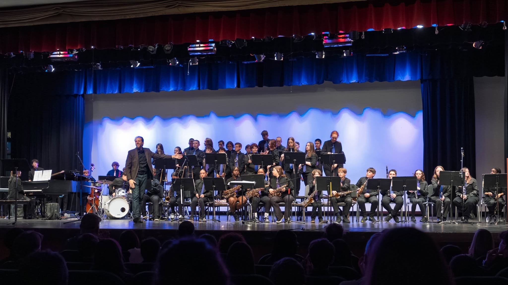 A school band performing on stage with students playing various instruments and a conductor leading them.