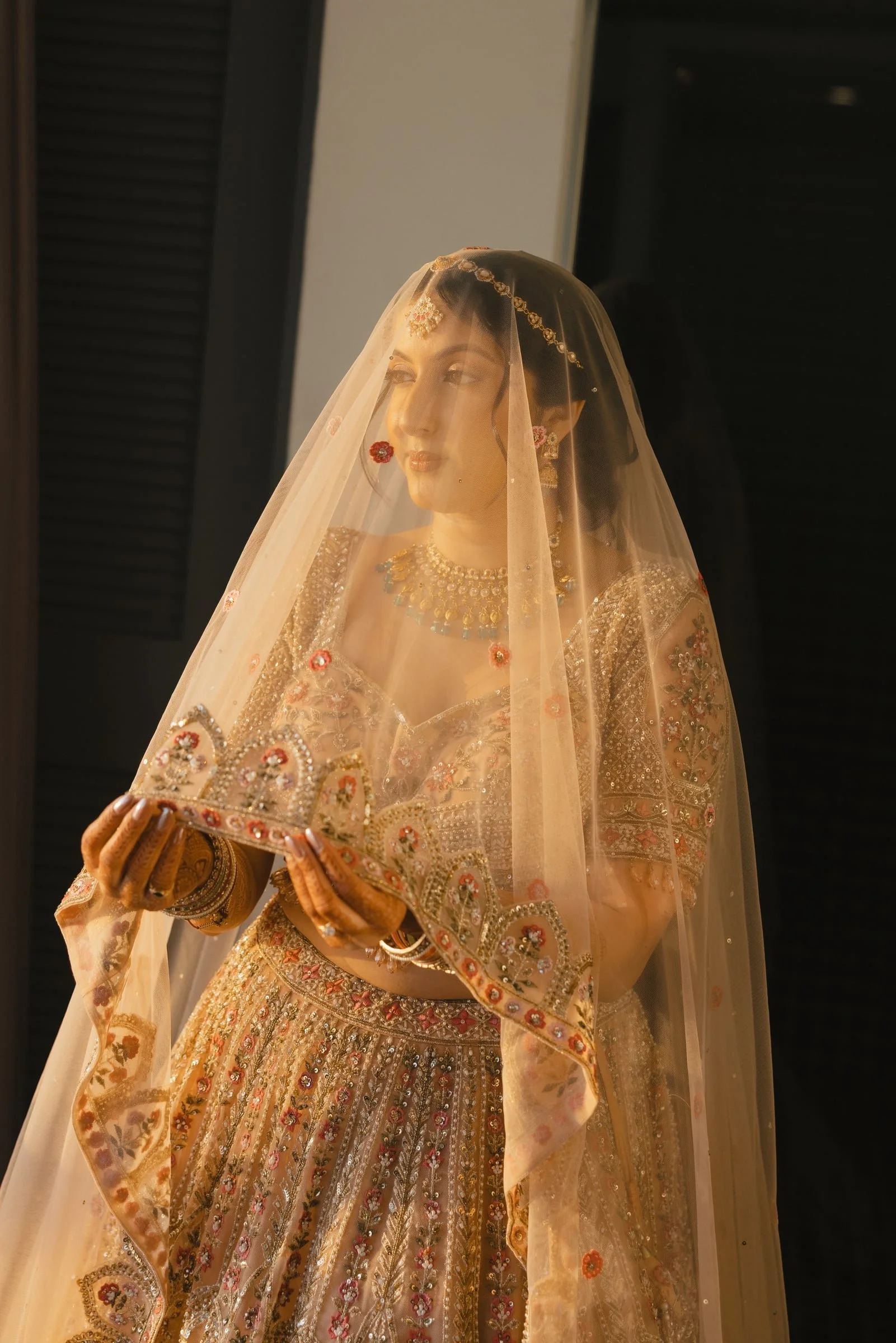 A woman dressed in traditional Indian bridal attire, holding a decorated tray, wearing jewelry, a veil, and elaborate clothing.