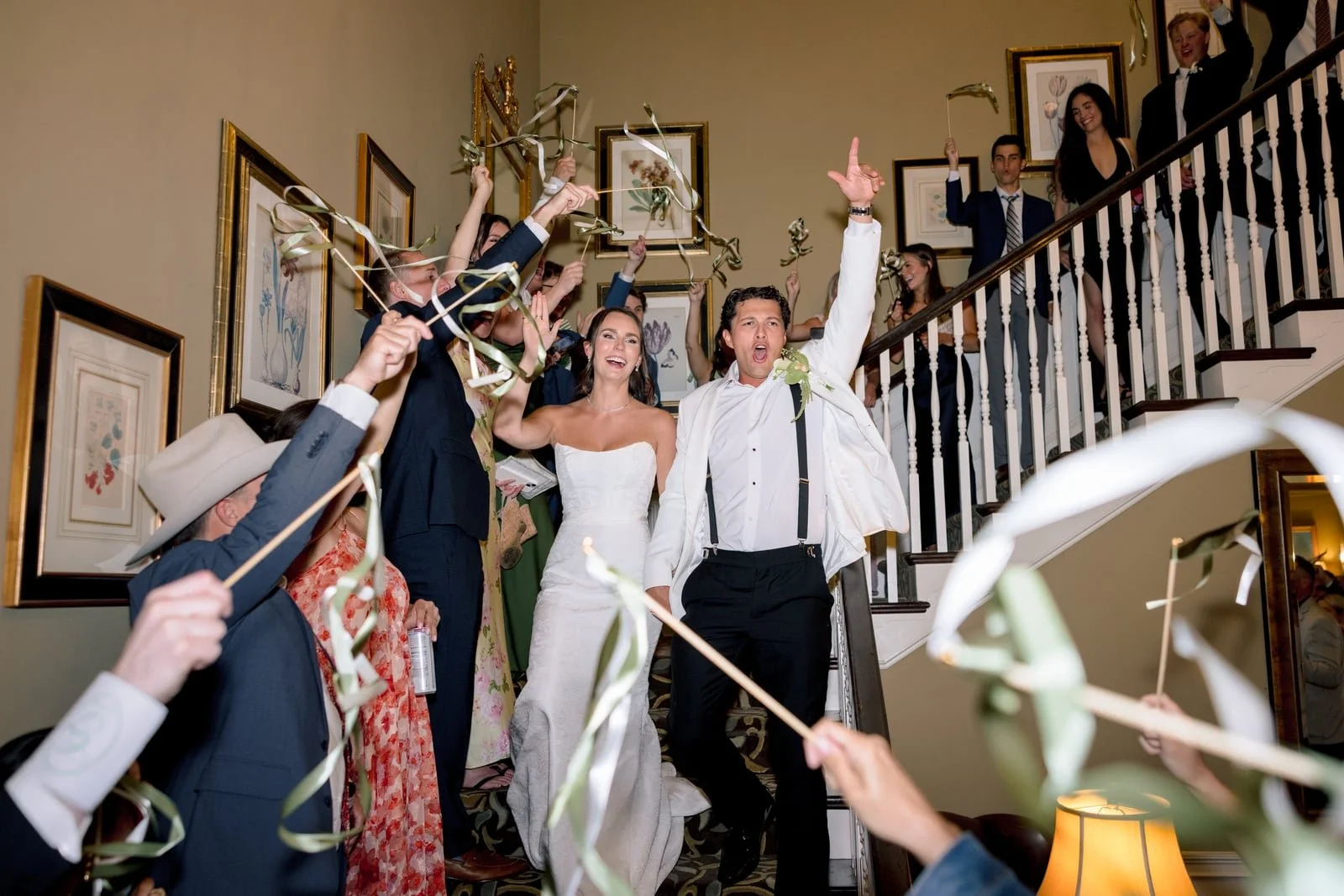 Wedding celebration with the bride and groom at the center, surrounded by friends and family holding streamers and cheerfully celebrating on a staircase.