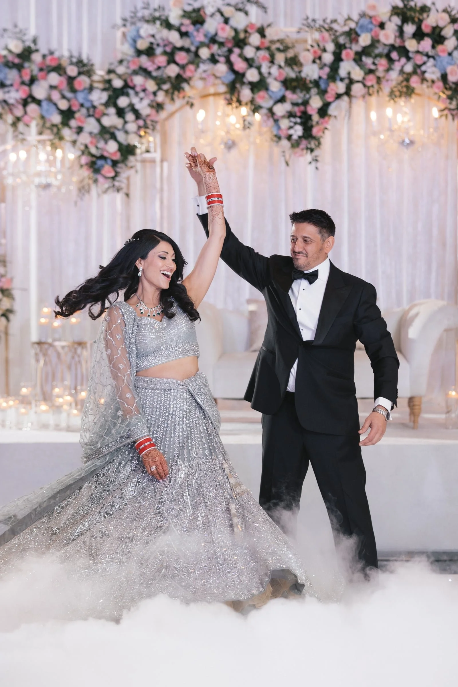 A bride and groom dancing at their wedding reception, with floral decorations and fairy lights in the background.