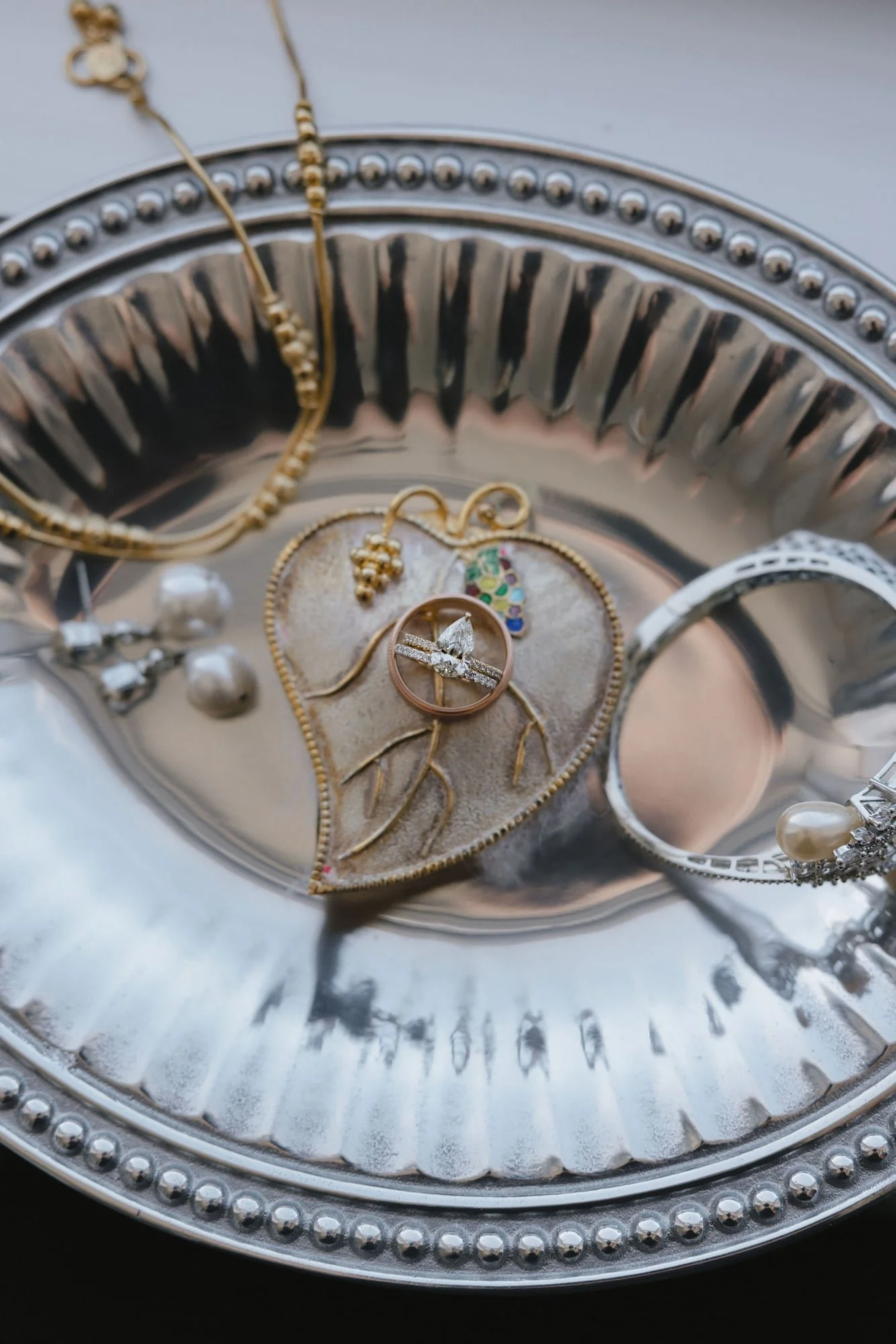Silver tray with jewelry including a diamond ring, necklaces, bracelets, and earrings displayed on a reflective surface.