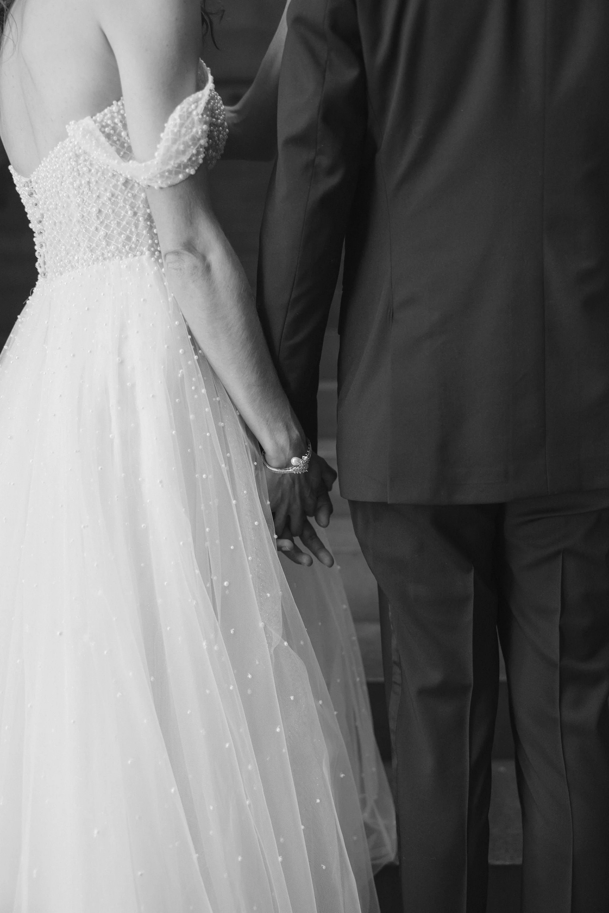 Close-up of a bride and groom holding hands during a wedding ceremony, black and white photo.