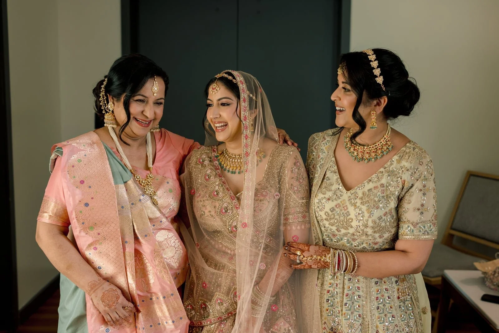 Three women in traditional Indian attire smiling and sharing a joyful moment