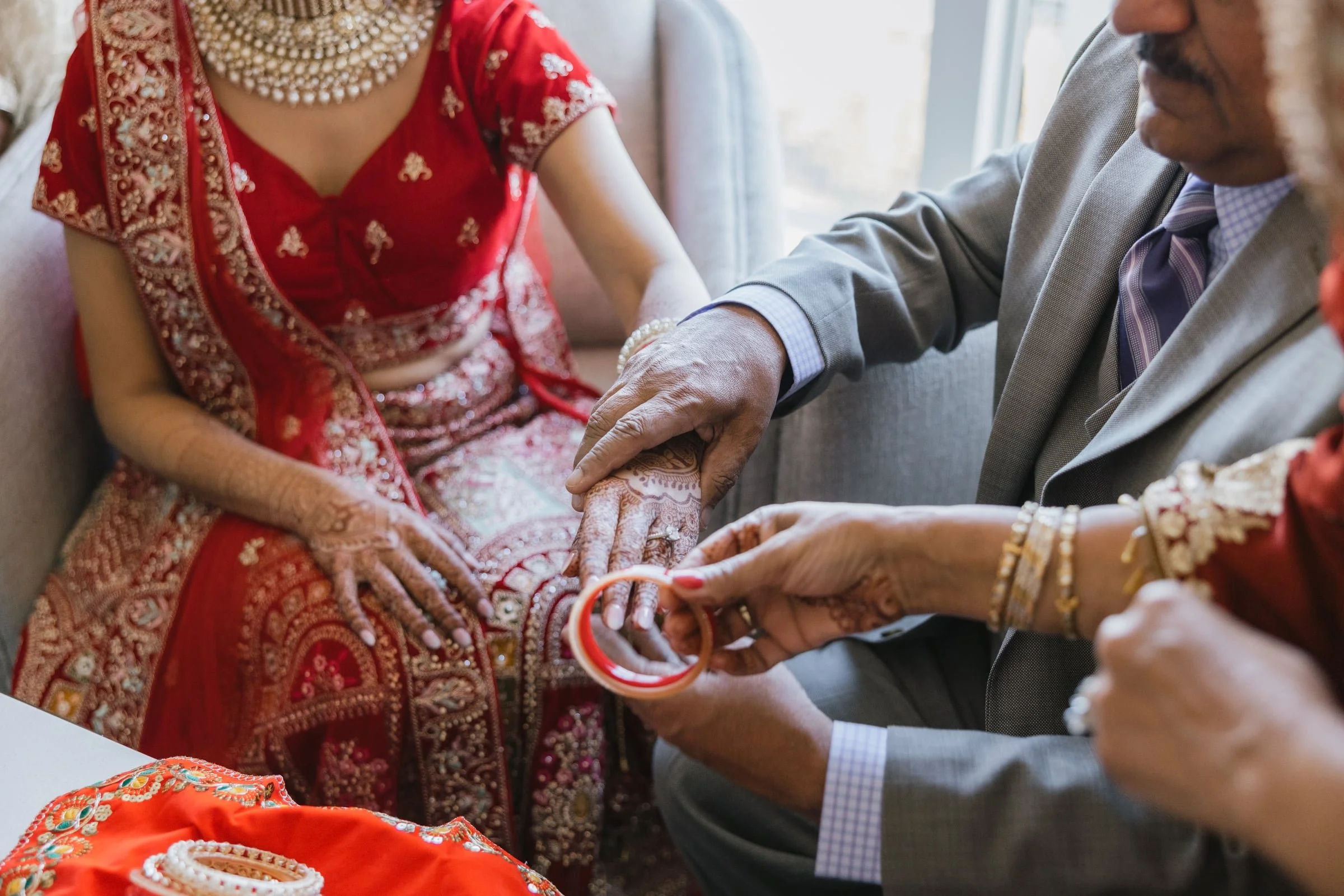 Close-up of bridal henna ceremony, featuring women in traditional Indian attire and jewelry, with hands decorated with henna designs.