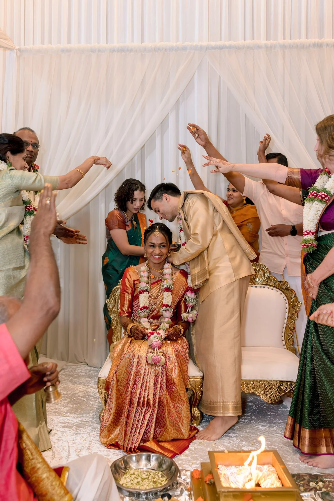 Hindu wedding ceremony with bride and groom seated, surrounded by relatives performing rituals, candles, and flowers