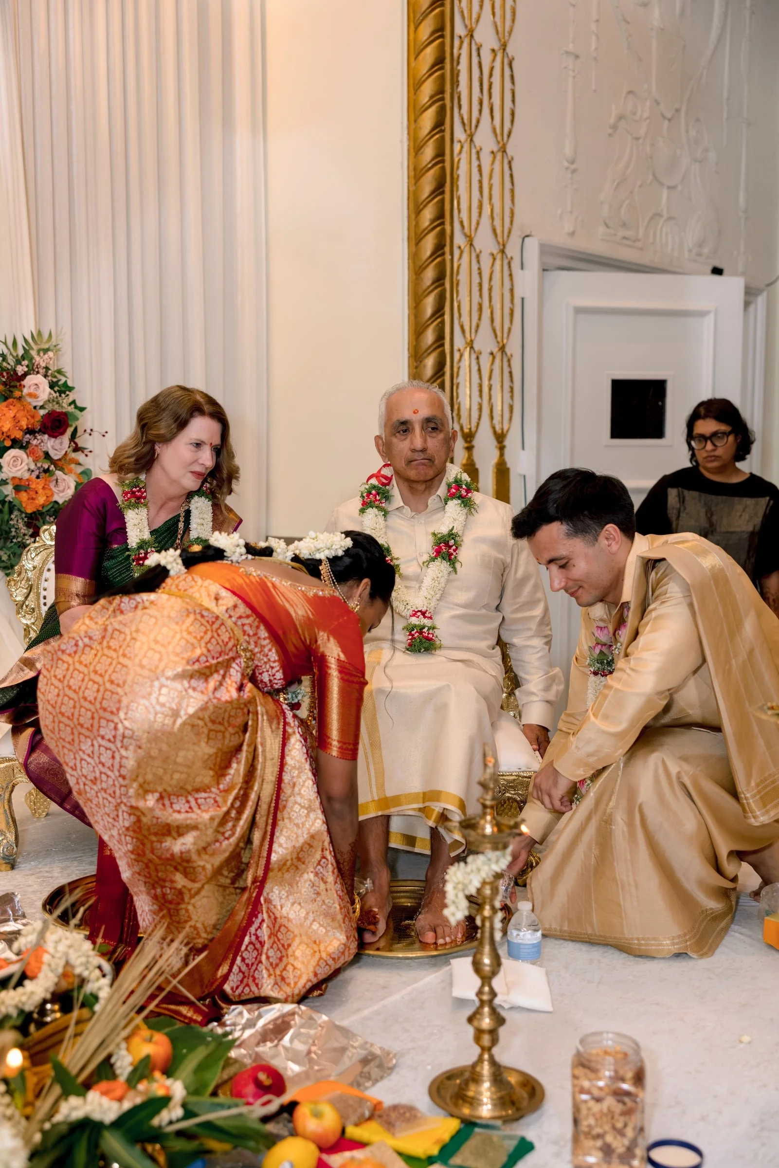 Indian temple ceremony with men and women in traditional attire, floral garlands, offerings, and sacred items.
