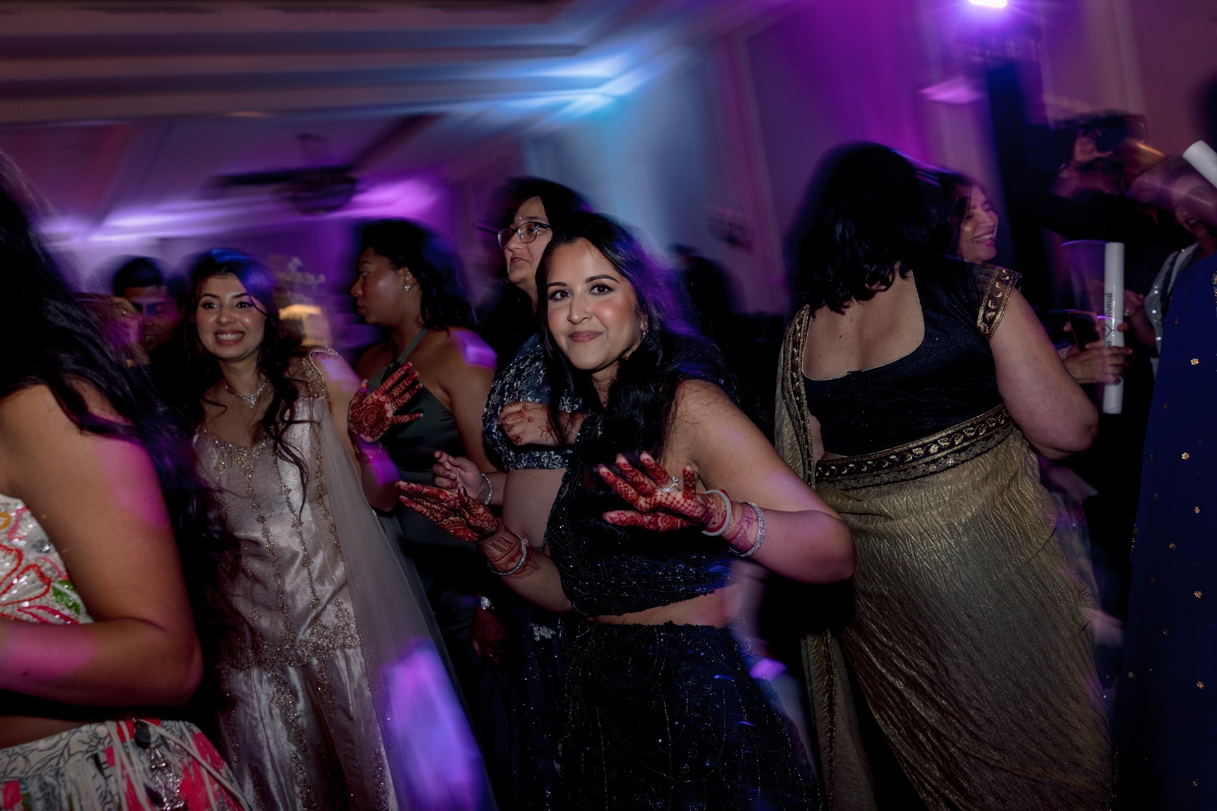 Group of women dancing and smiling at a celebration or party, illuminated by colorful lights.