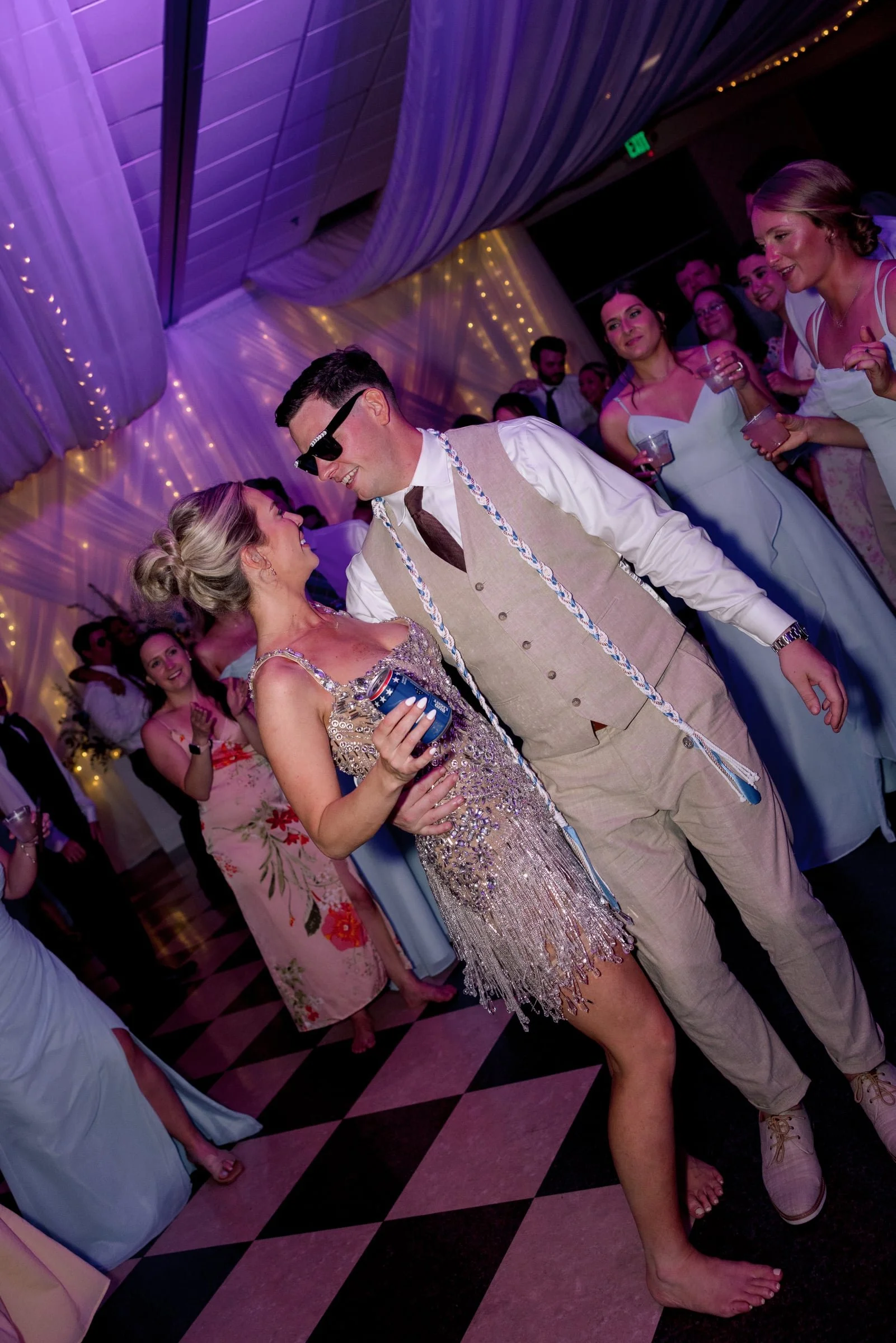 People dancing at a party with purple and pink lighting and draped fabric ceiling.