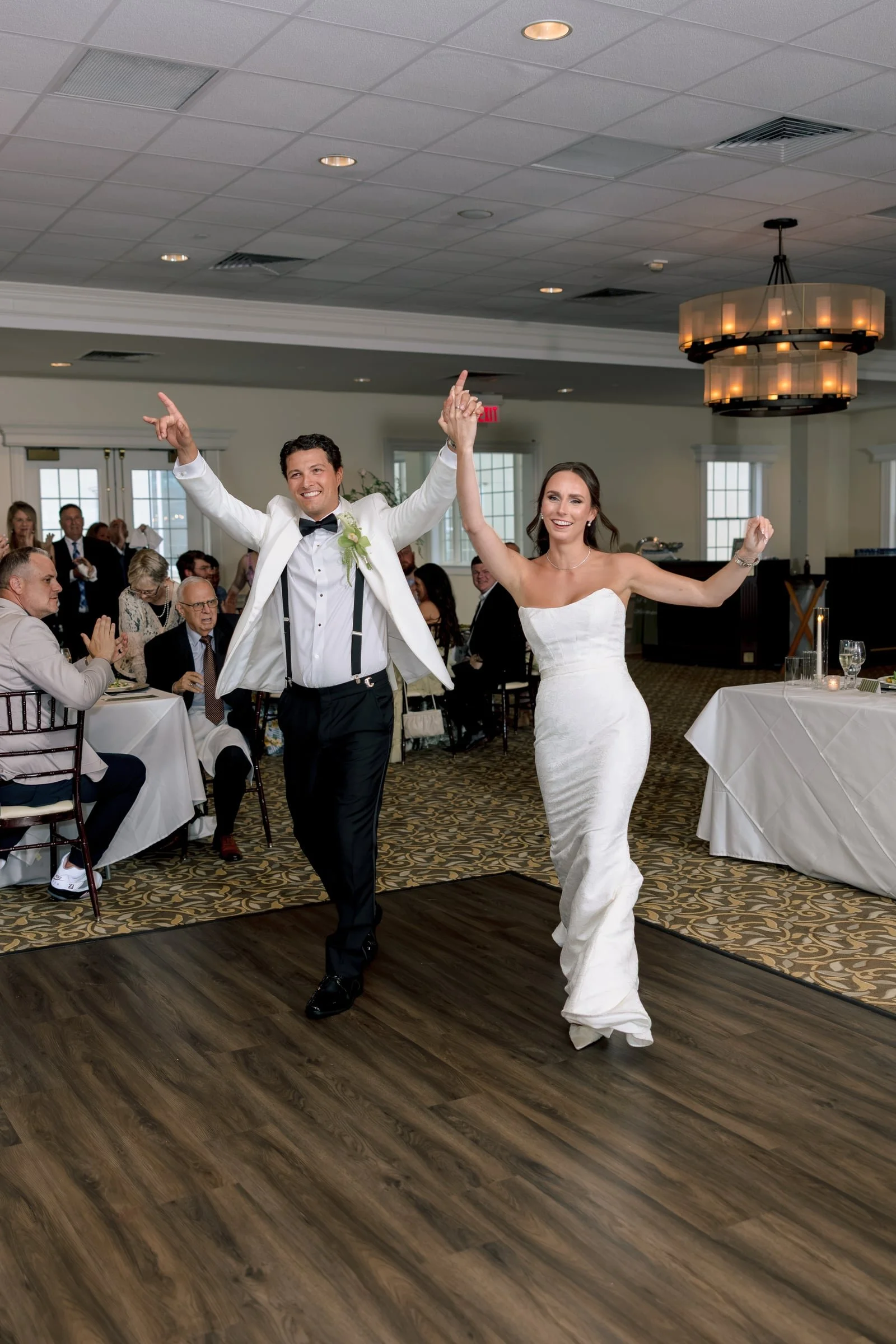 A bride and groom dancing and celebrating at their wedding reception inside a decorated banquet hall.