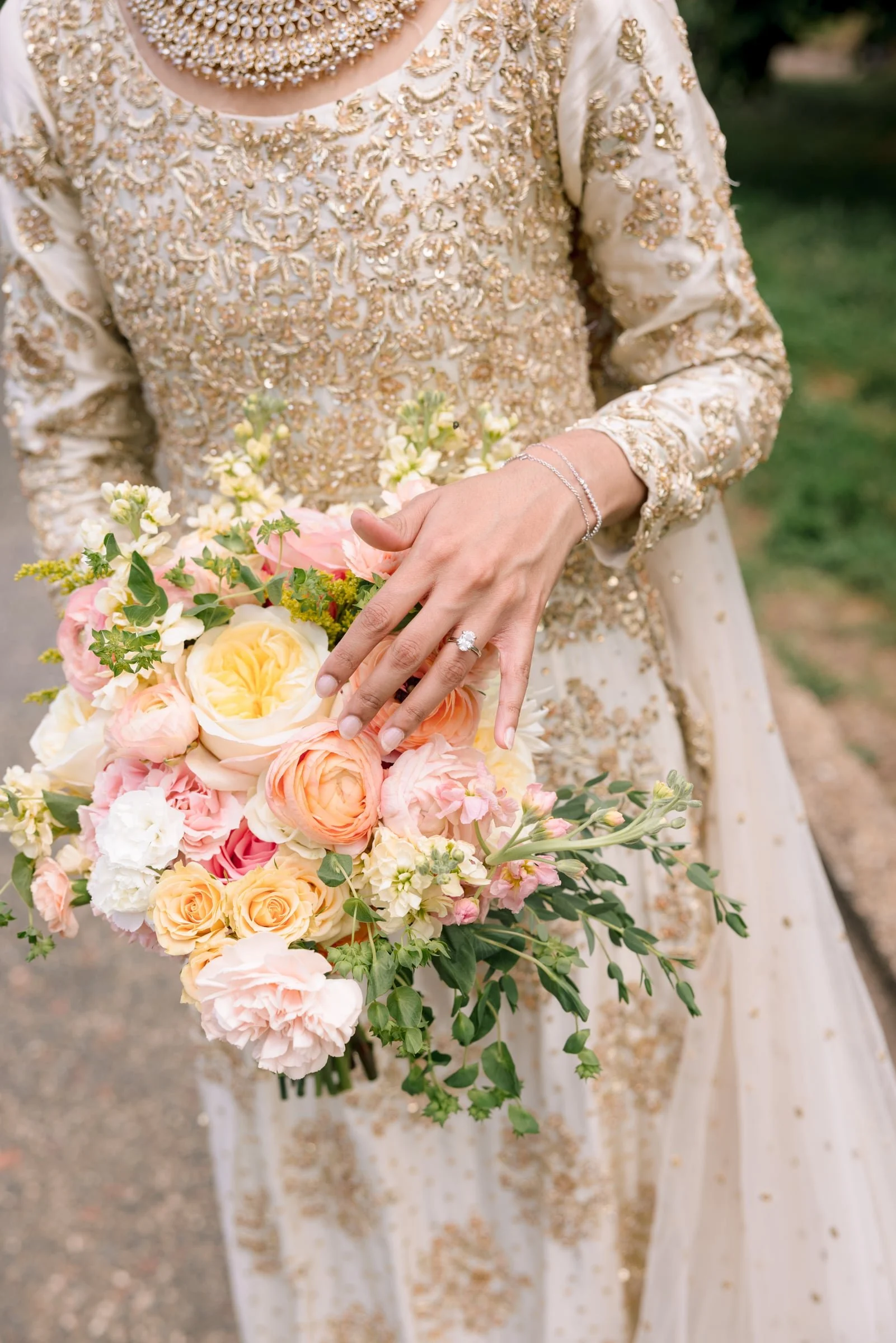 A person wearing an embroidered cream-colored dress holding a bouquet of pink, yellow, and white flowers.