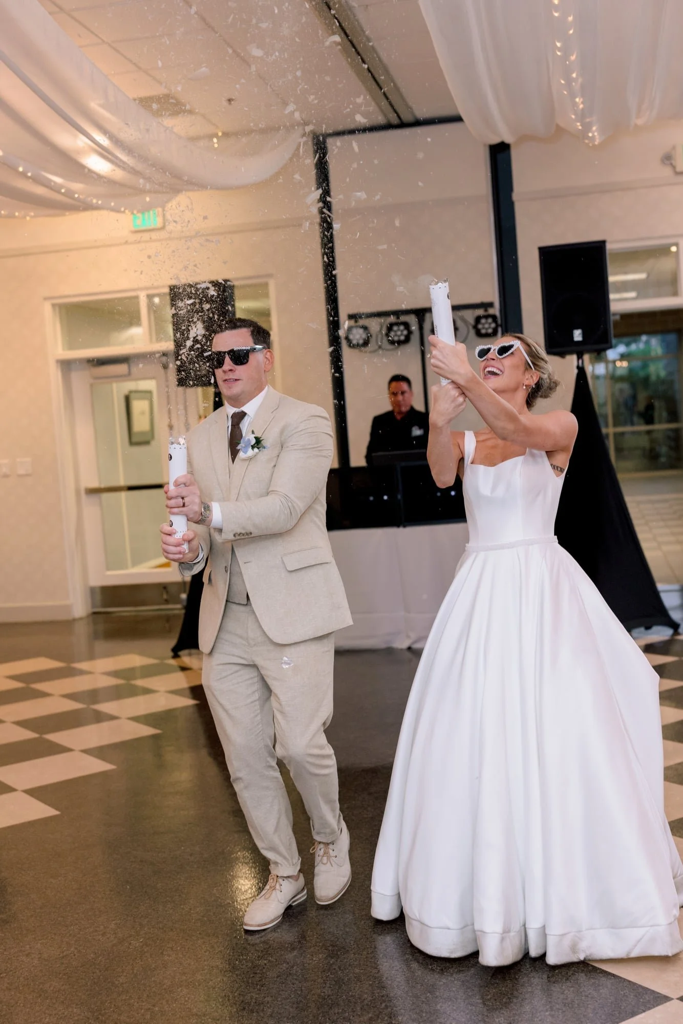 People celebrating with party poppers indoors at a wedding reception, dressed in formal attire, with a woman in a white wedding dress and a man in a beige suit.