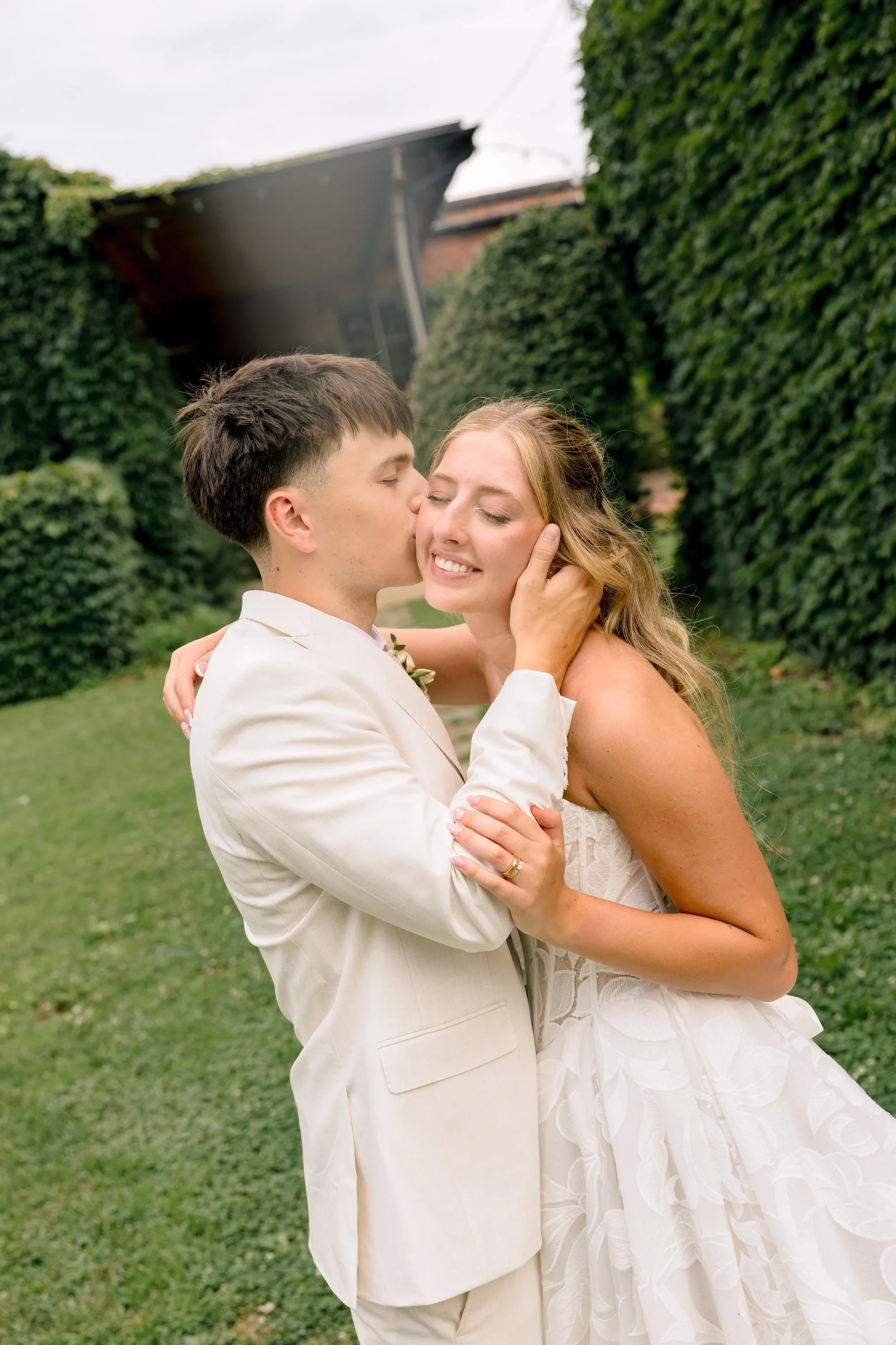 A bride and groom hugging and smiling in an outdoor setting surrounded by greenery.