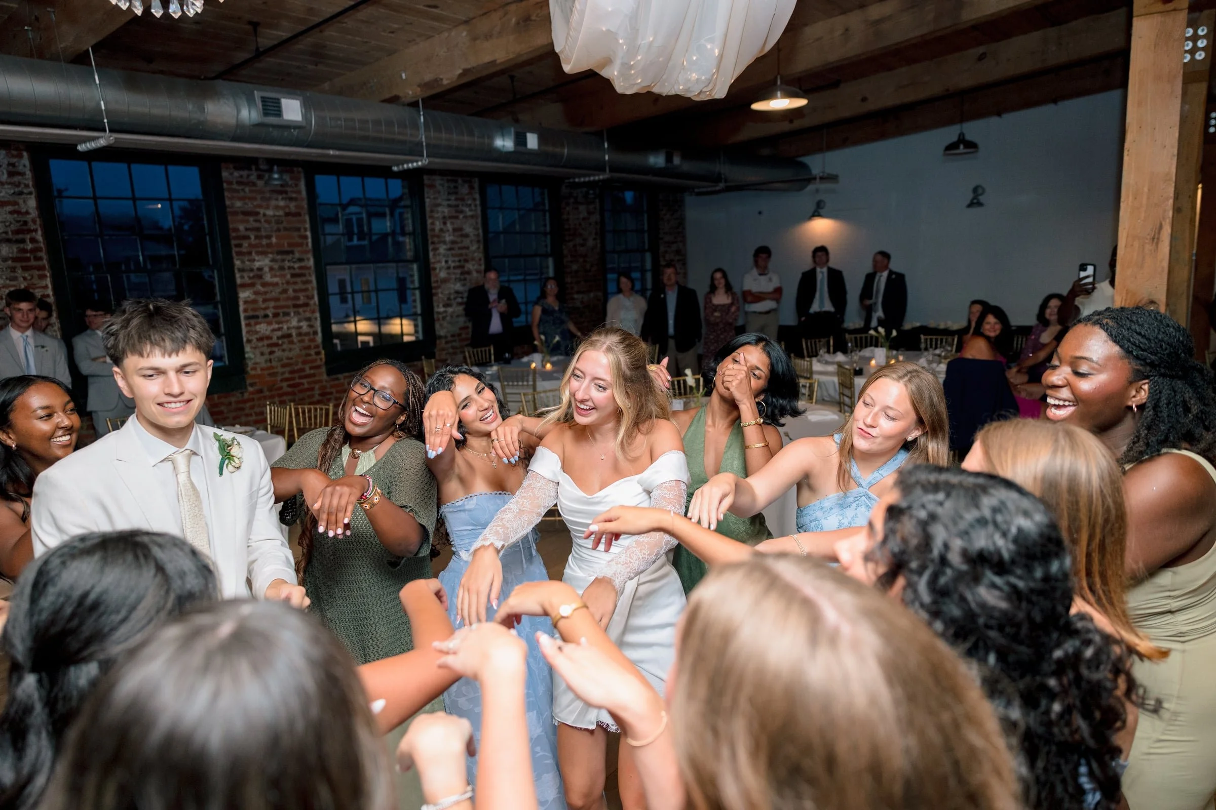 People dancing and celebrating at a wedding reception in a rustic indoor venue.