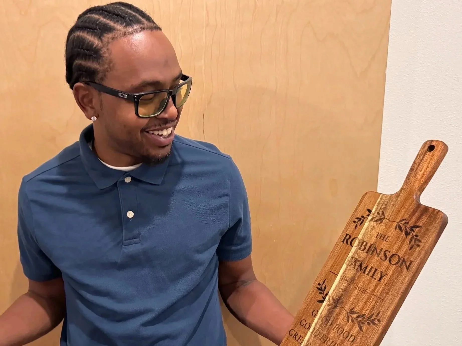 Maker holding a personalized engraved family cutting board with custom family name and decorative botanical details.