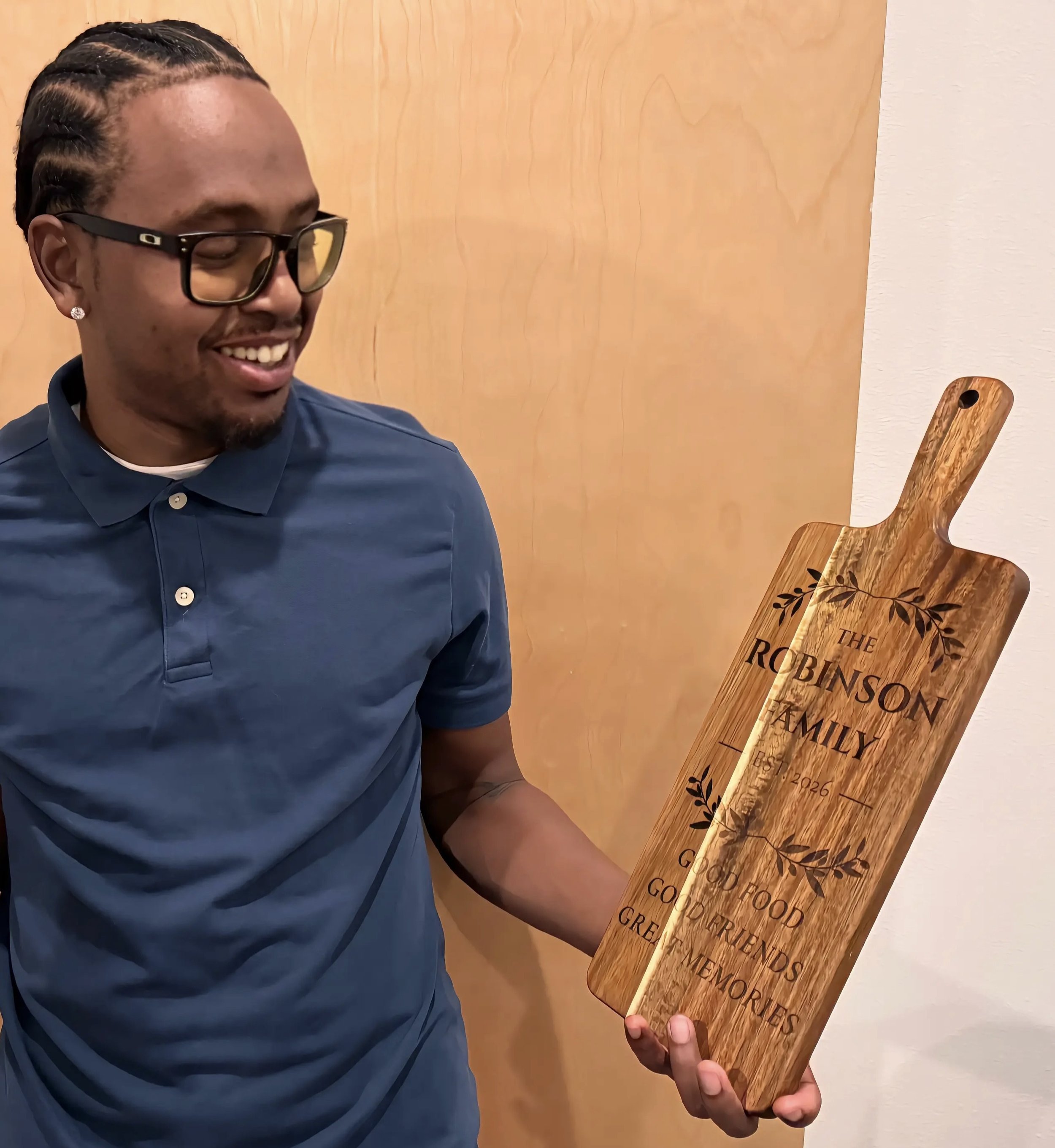 Maker holding a personalized engraved wooden cutting board featuring the Robinson family name and decorative leaf details.