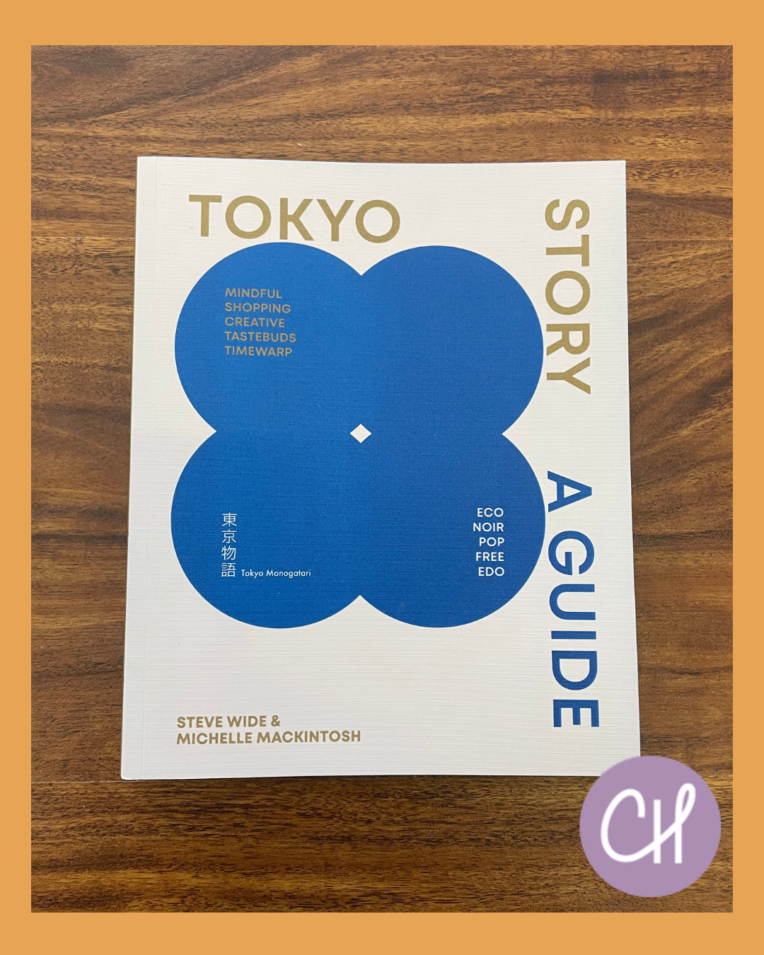 Book titled 'Tokyo A Guide' by Steve Wide and Michelle Mackintosh, featuring a white cover with big blue circles and gold and blue text, placed on a wooden surface.