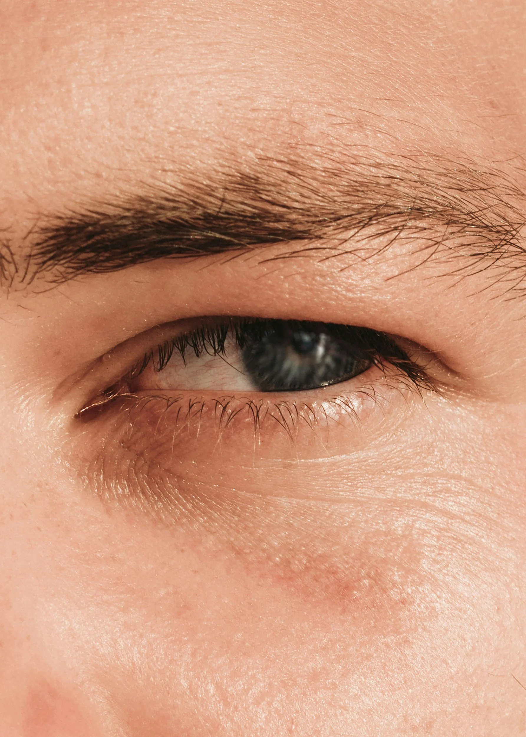 Close-up of a person's closed eye showing eyelash, eyebrow, and surrounding skin.