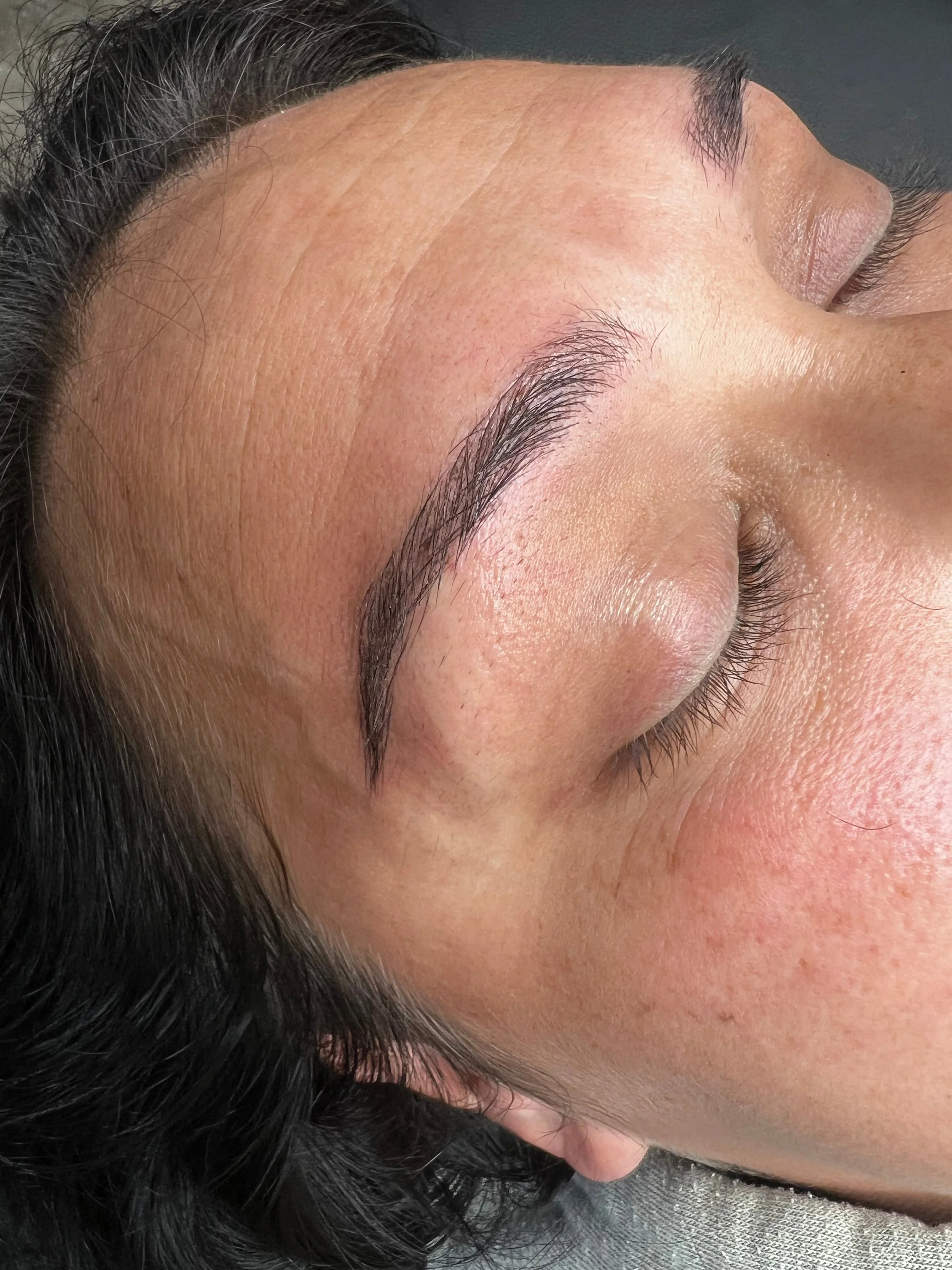 Close-up of a person's forehead, eyebrow, eyelid, and part of the face, showing natural skin texture and dark hair.