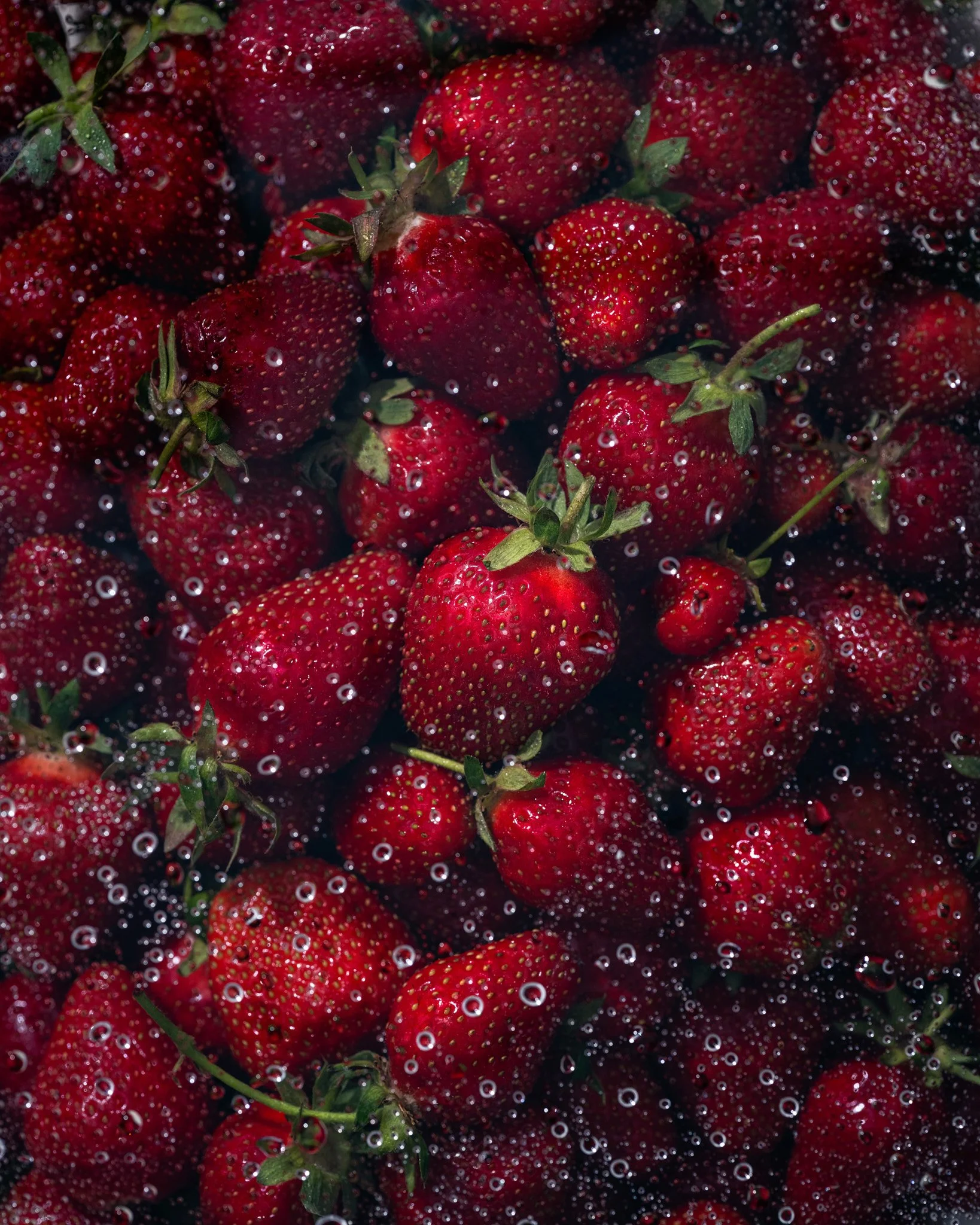 Creative food photography of fresh red strawberries submerged in water with bubbles, highlighting freshness, texture and vibrant natural color