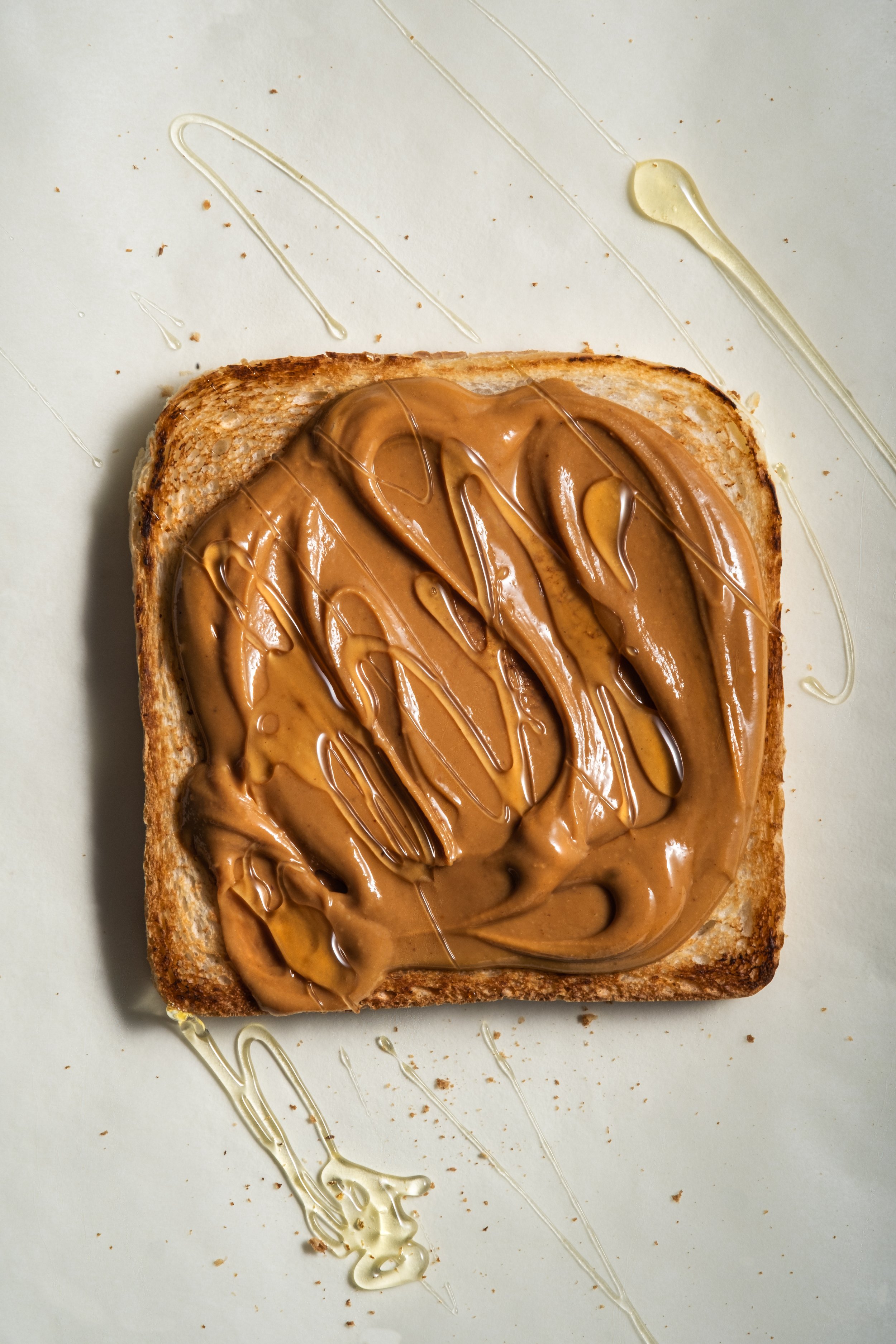 Top-view food photography of toasted bread generously spread with creamy peanut butter and drizzled with honey