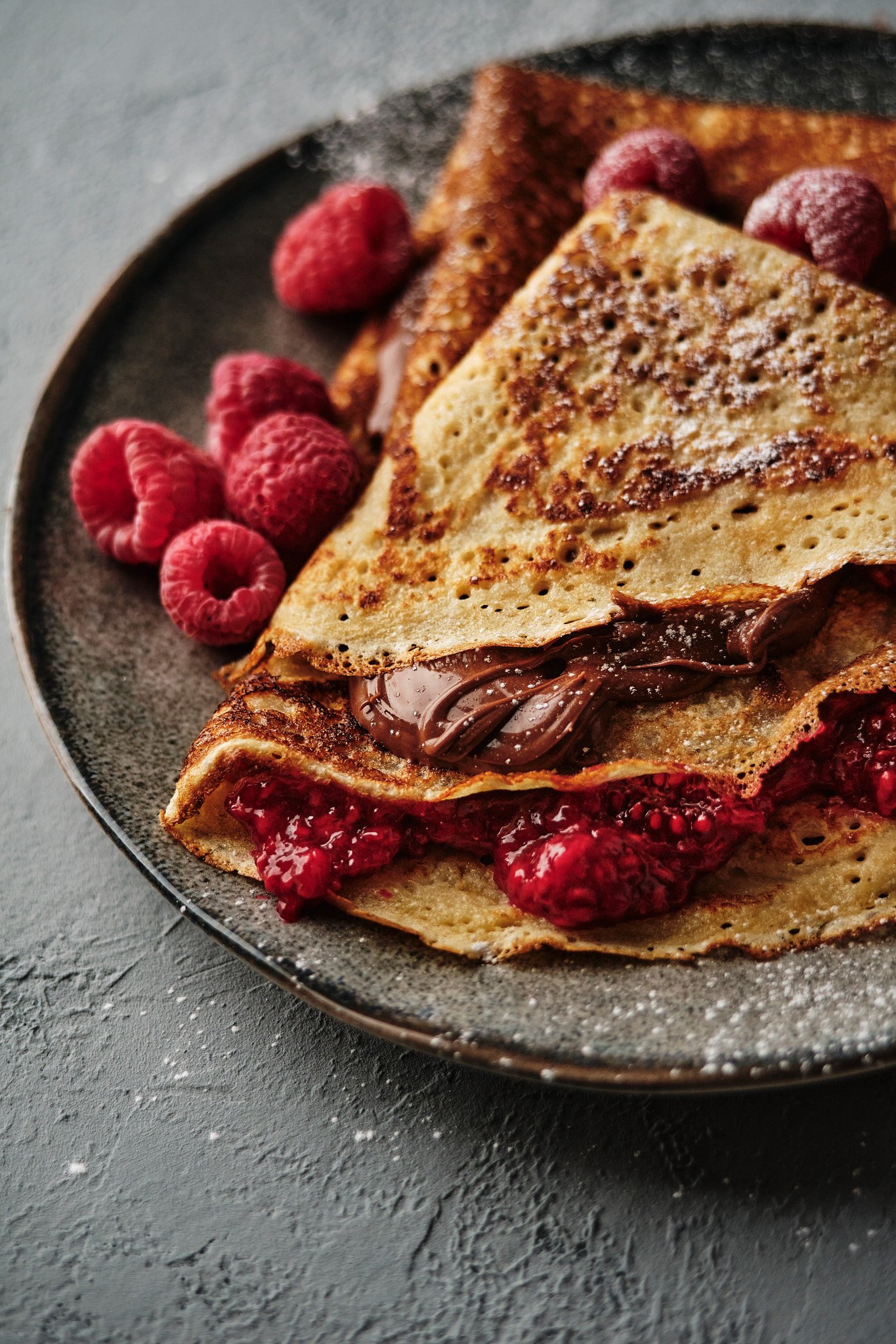 Professional dessert photography and food styling of crepes with chocolate, raspberry sauce and fresh berries, created for food brands, restaurants and commercial advertising