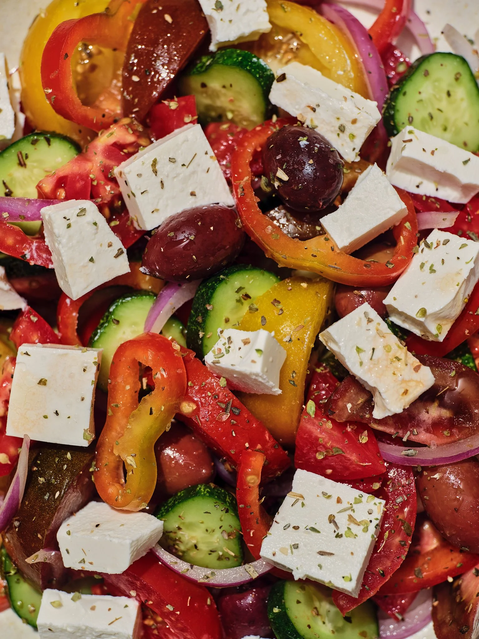 Close-up food photography of a colorful Greek salad with feta cheese, ripe tomatoes, cucumber, bell peppers, red onion, Kalamata olives and dried herbs