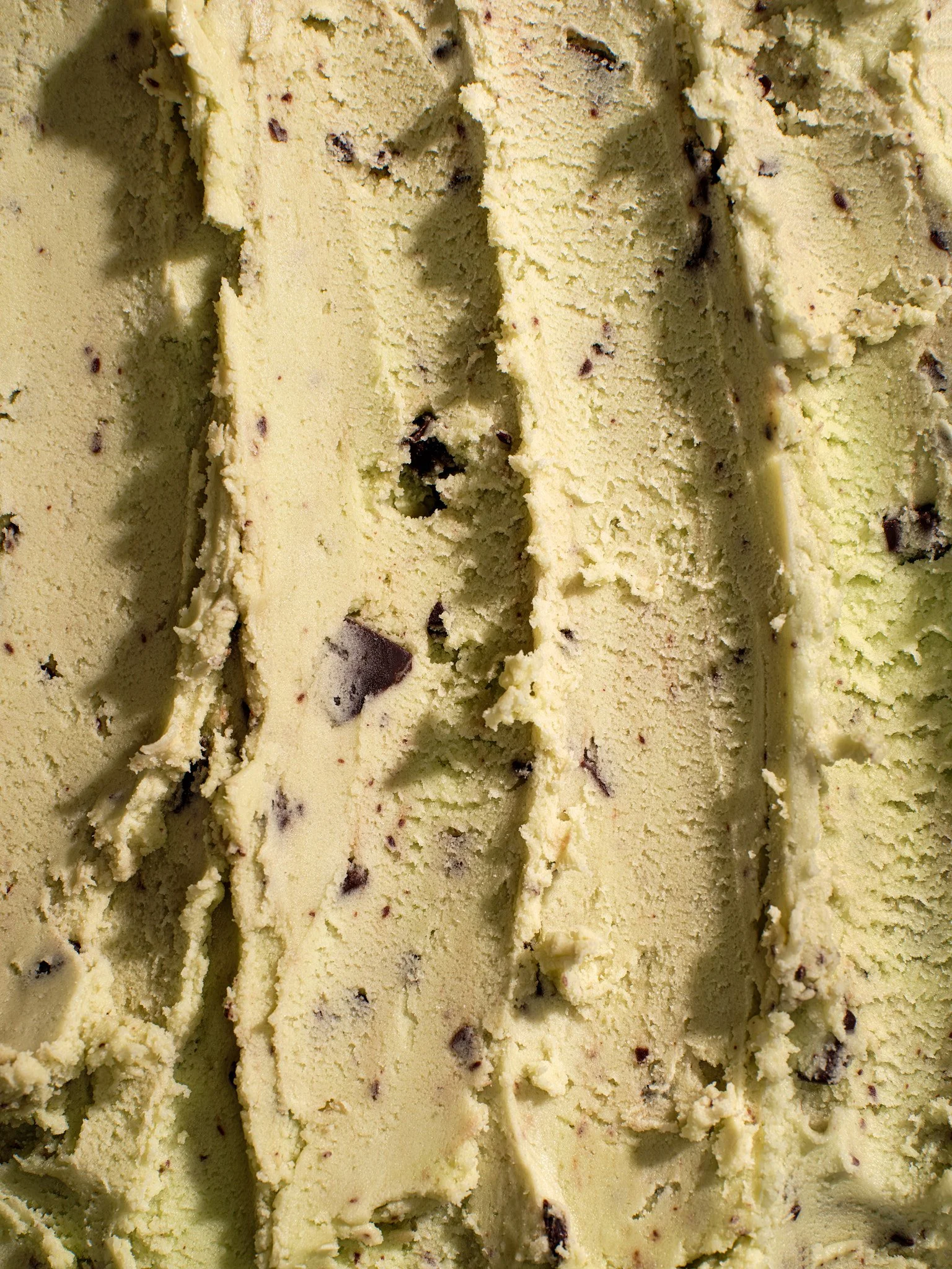 Macro food photography of creamy pistachio ice cream with chocolate chunks, showing rich texture and scoop marks