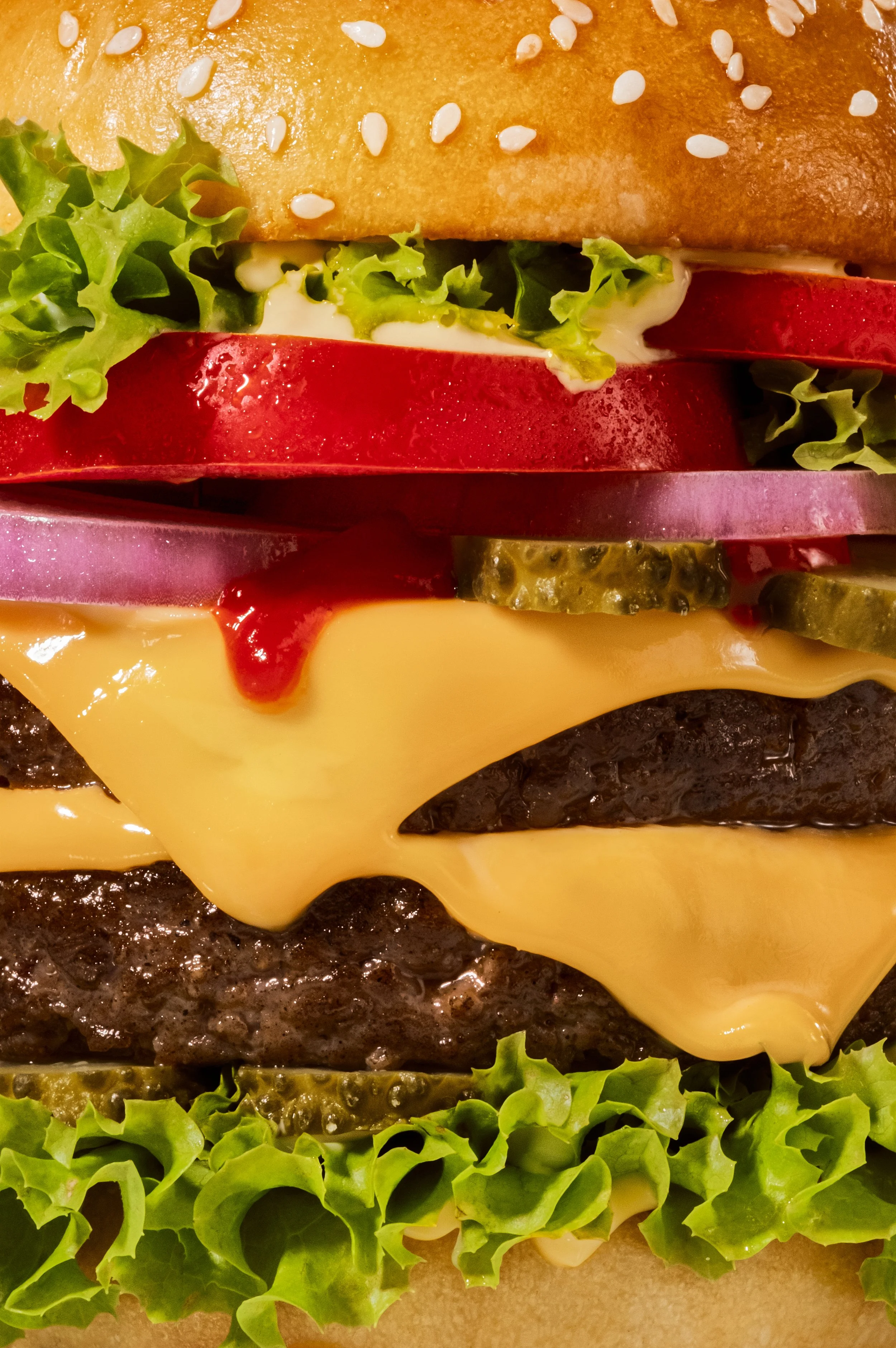 Close-up of a cheeseburger with lettuce, tomato, pickles, onion, cheese, a beef patty, and a sesame seed bun.