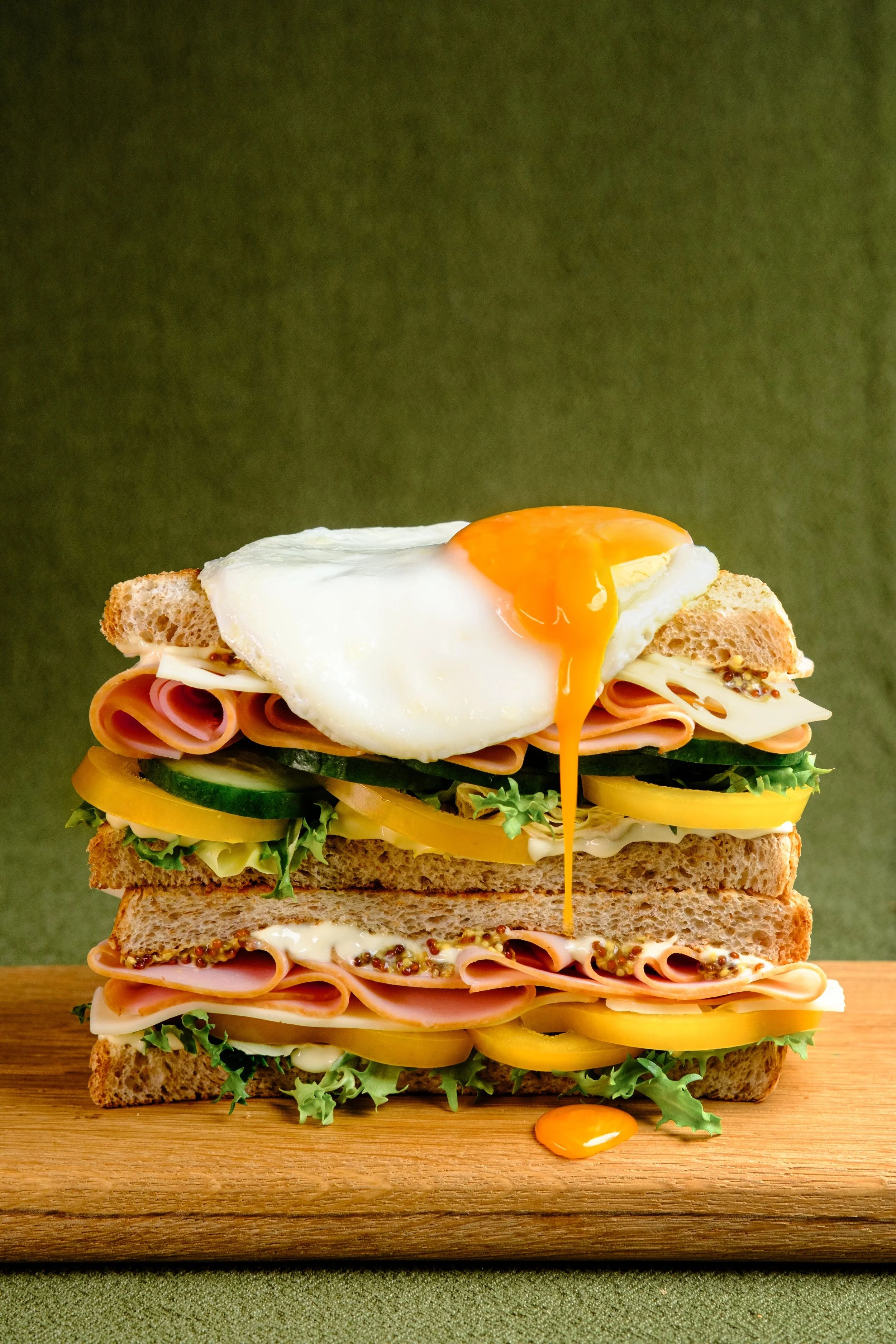 Commercial food photography and food styling of a stacked club sandwich with ham, cheese, fresh vegetables and a fried egg, created for food brands, restaurants and advertising campaigns