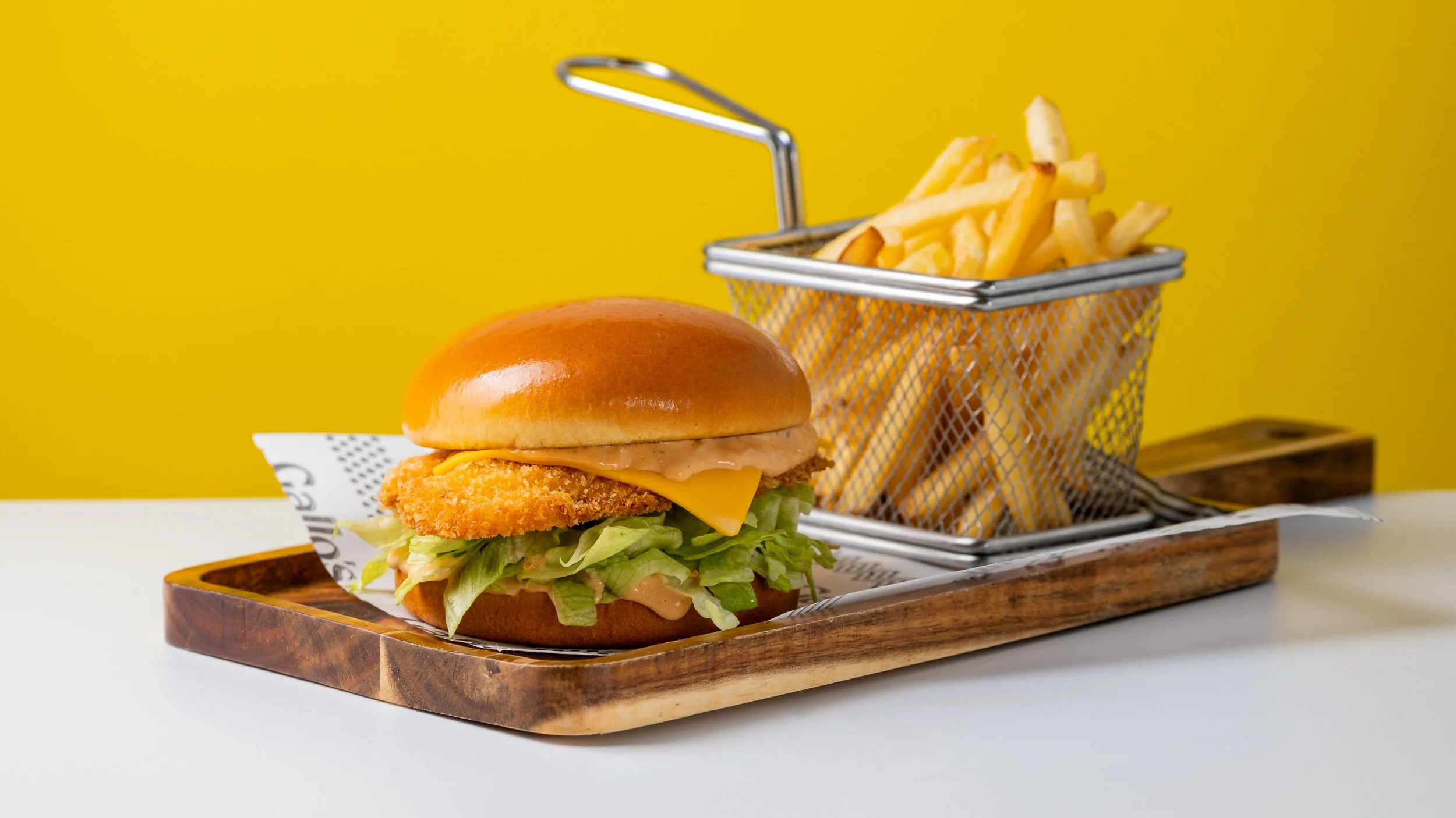 Commercial restaurant food photography and food styling of a crispy chicken burger with cheese, lettuce and French fries, created for menus, delivery platforms and advertising campaigns