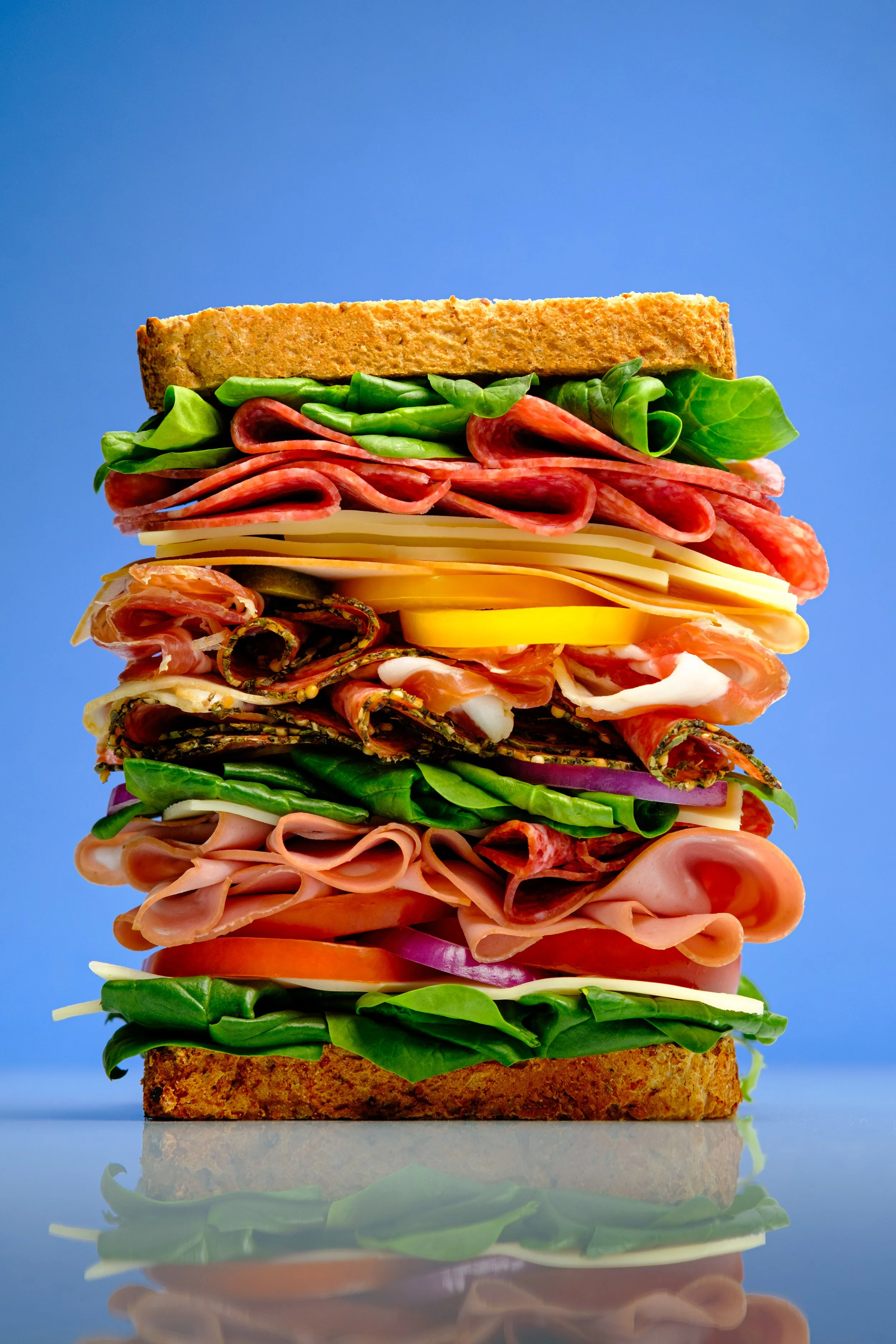 Commercial food photography and food styling of a layered deli sandwich with cured meats, cheese and fresh vegetables, created for food brands, restaurants and advertising campaigns