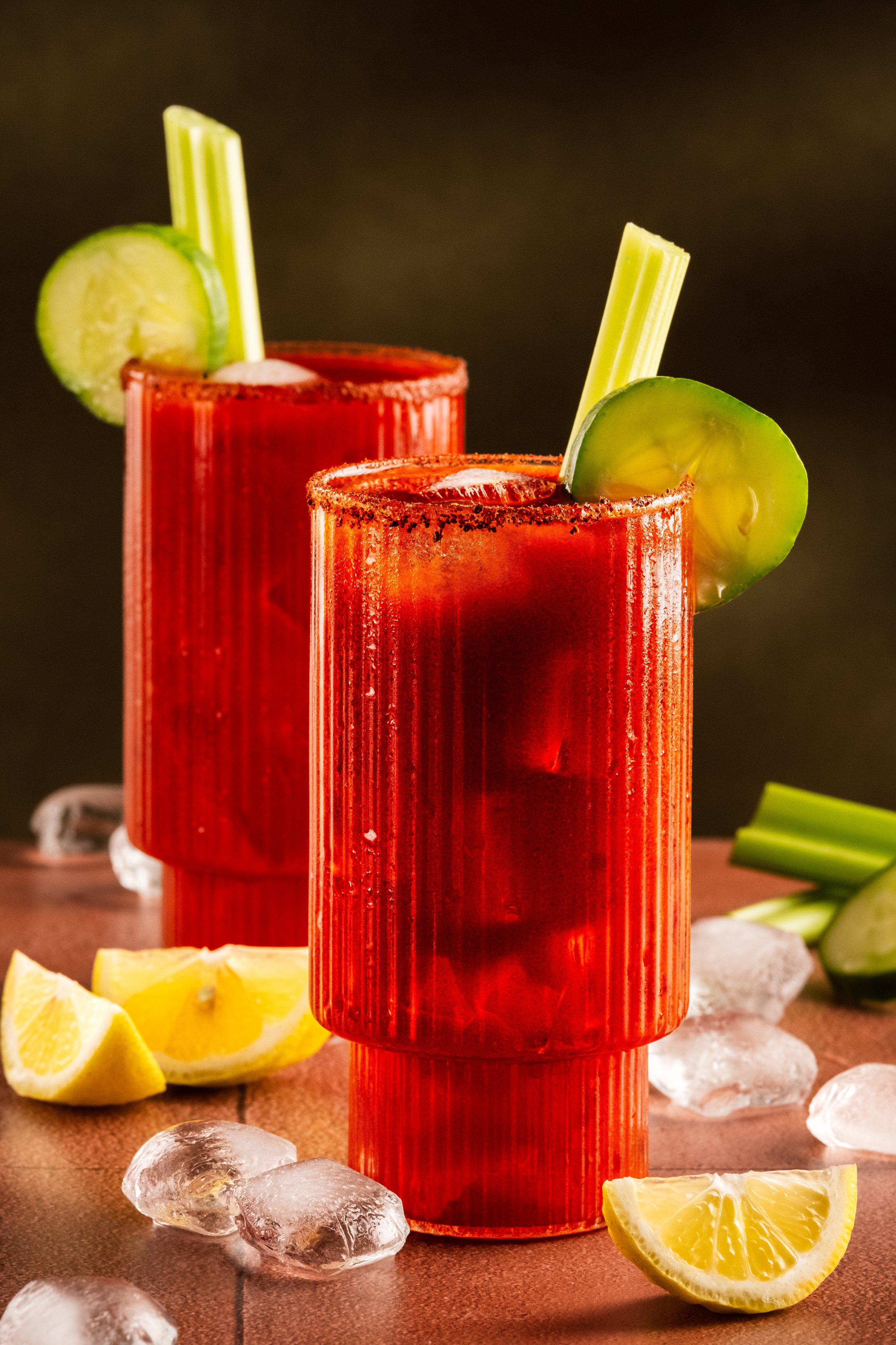 Commercial beverage photography of two Bloody Mary cocktails garnished with celery and cucumber, styled with ice, lemon and a spiced rim for bars, restaurants and advertising