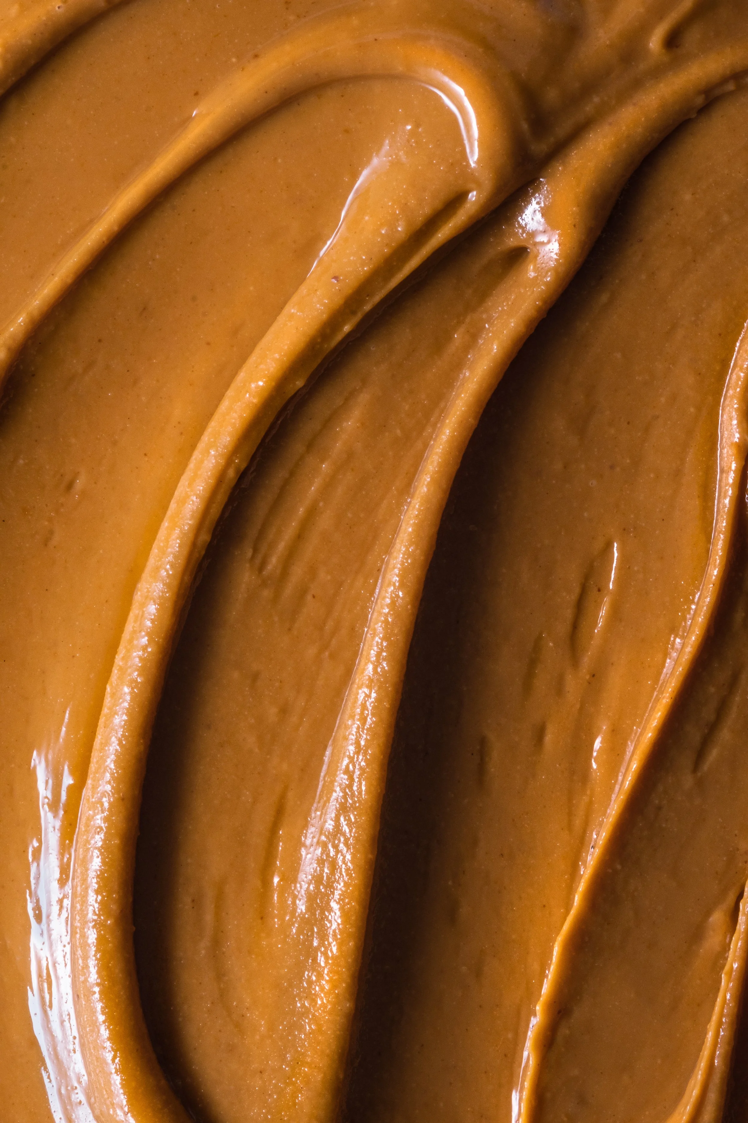 Macro food photography of smooth creamy peanut butter with glossy swirls and rich golden-brown texture