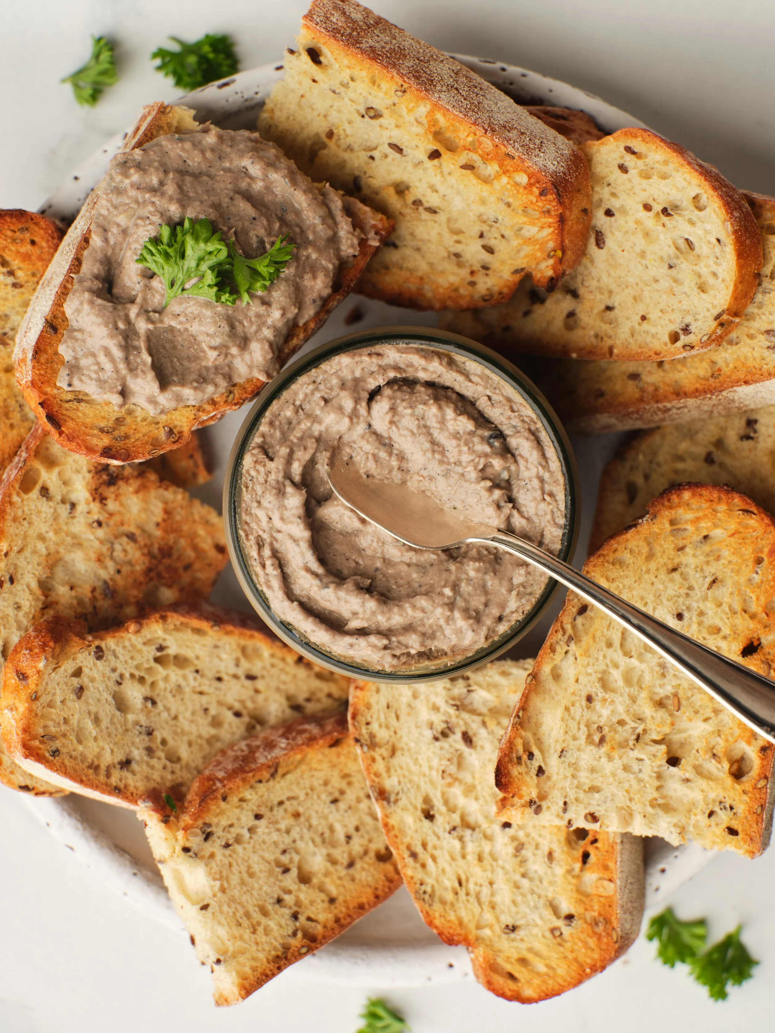 Top-view food photography of creamy pâté served with slices of toasted artisan bread and garnished with fresh parsley
