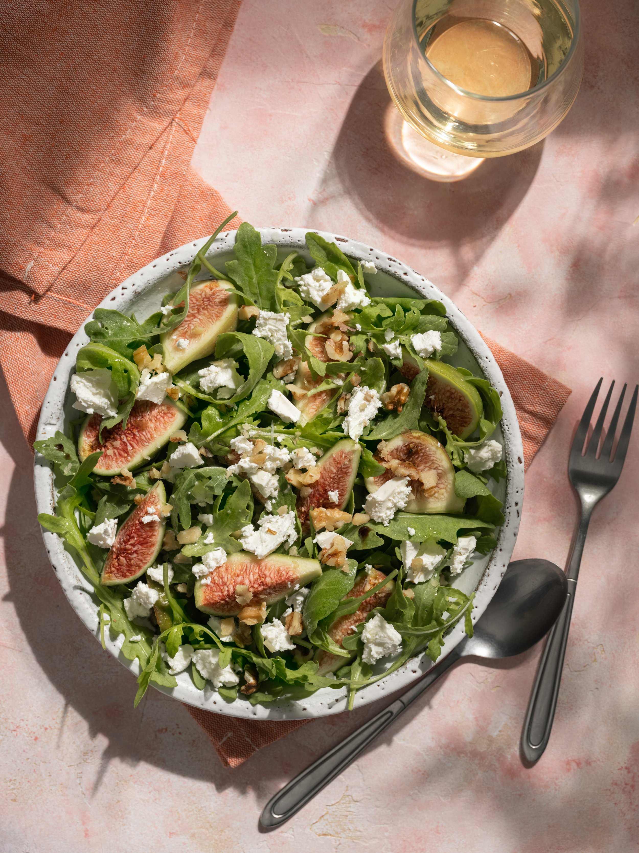 Professional food photography of a fresh salad with figs, arugula, feta cheese and walnuts, styled in natural sunlight for restaurants, food brands and editorial content